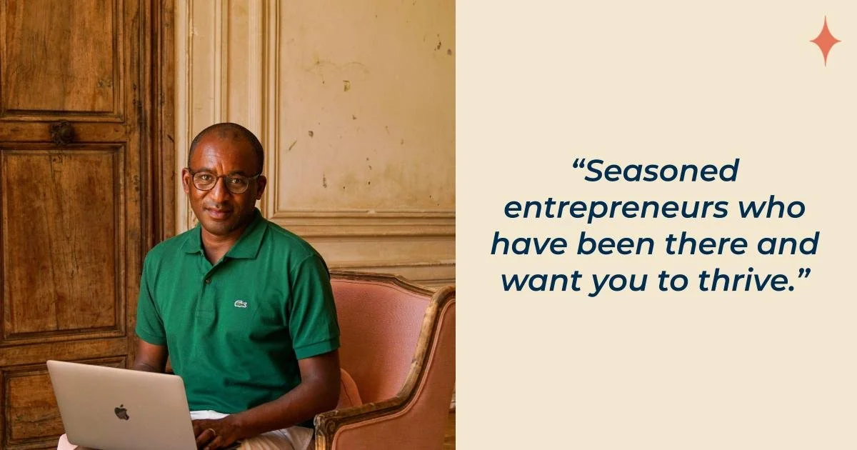 A man wearing glasses and a green polo shirt sitting at a table with a silver MacBook in front of him, in a room with wooden paneling and classical decor.