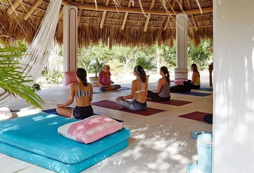 Group of women practicing yoga in a thatched-roof open-air pavilion surrounded by greenery during the daytime.