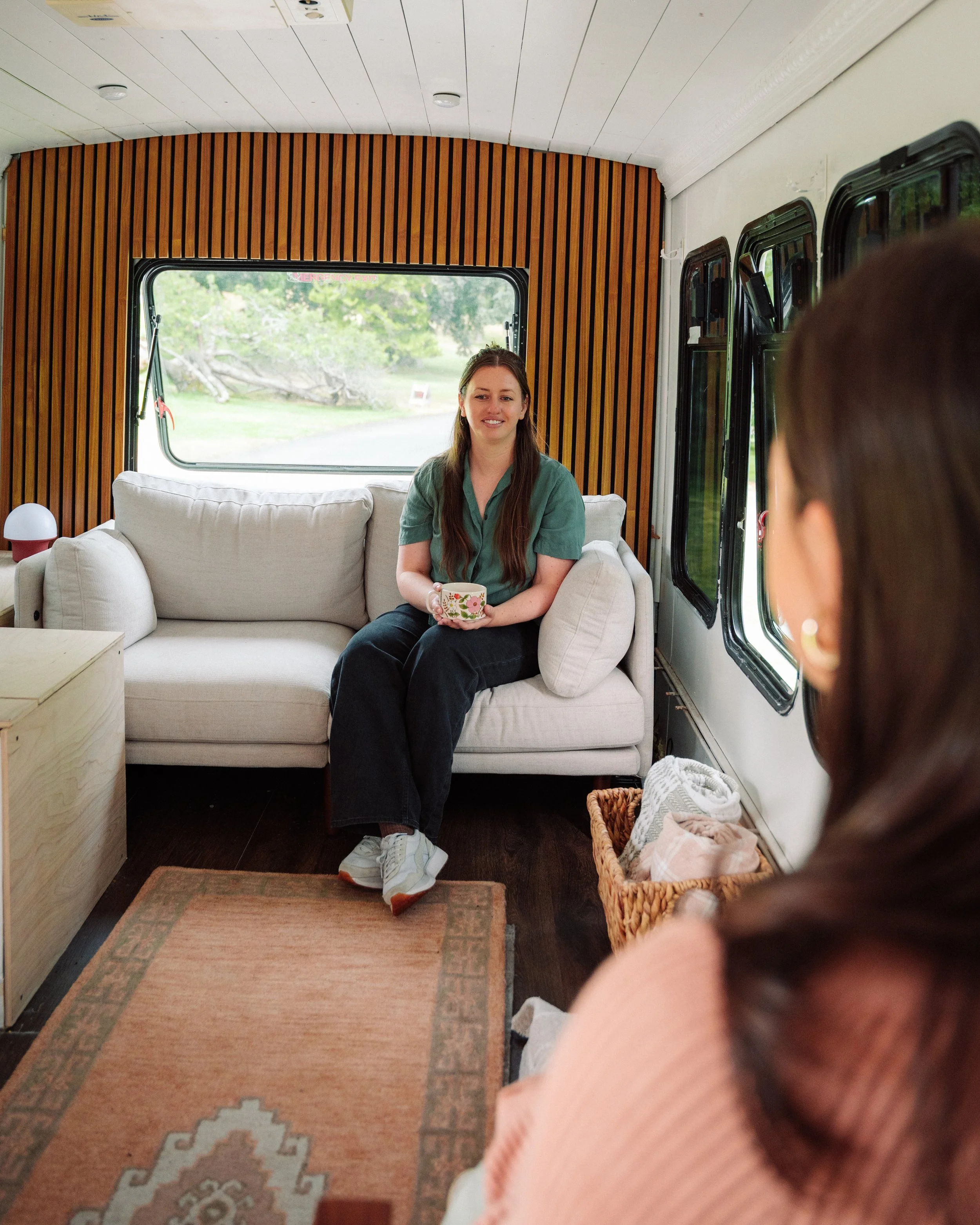 A mom sits inside a mobile therapy office and receives therapy. The interior features wooden paneling, windows, and a woven basket of towels.