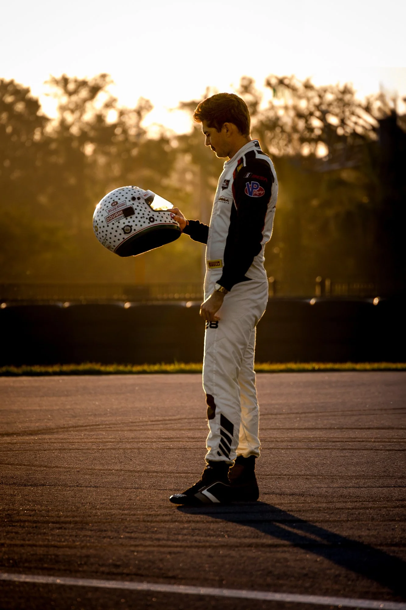 Driver in a racing suit holding a helmet on the track at sunrise at The Motor Enclave in Tampa, Florida.