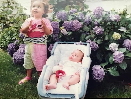 Baby and toddler in front of hydrangea bushes