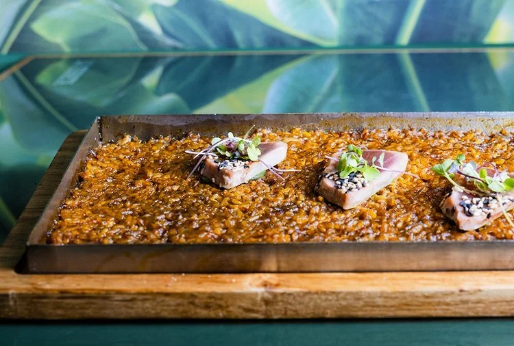 Plato de carne con arroz y verduras, decorado con microgreens, en una bandeja de madera