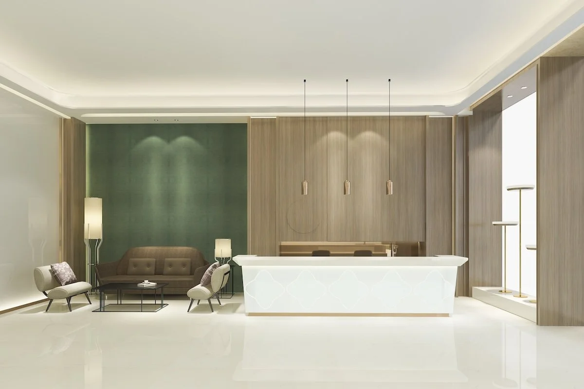 Modern hotel lobby with a reception desk, brown sofa, armchairs, green accent wall, pendant lights, and floor lamps.
