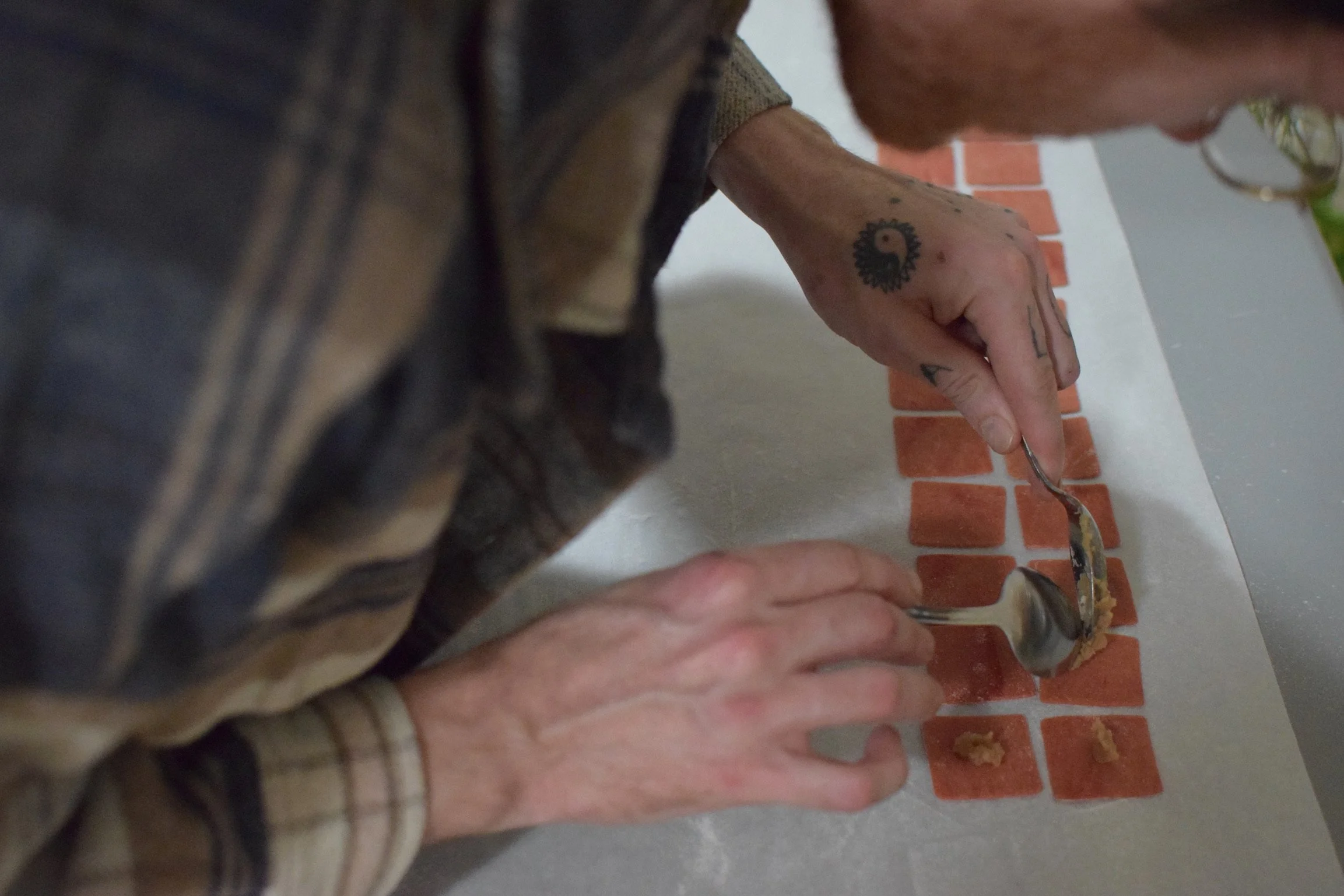 Person making pasta by placing small pieces of dough on a floured surface with a silver spoon