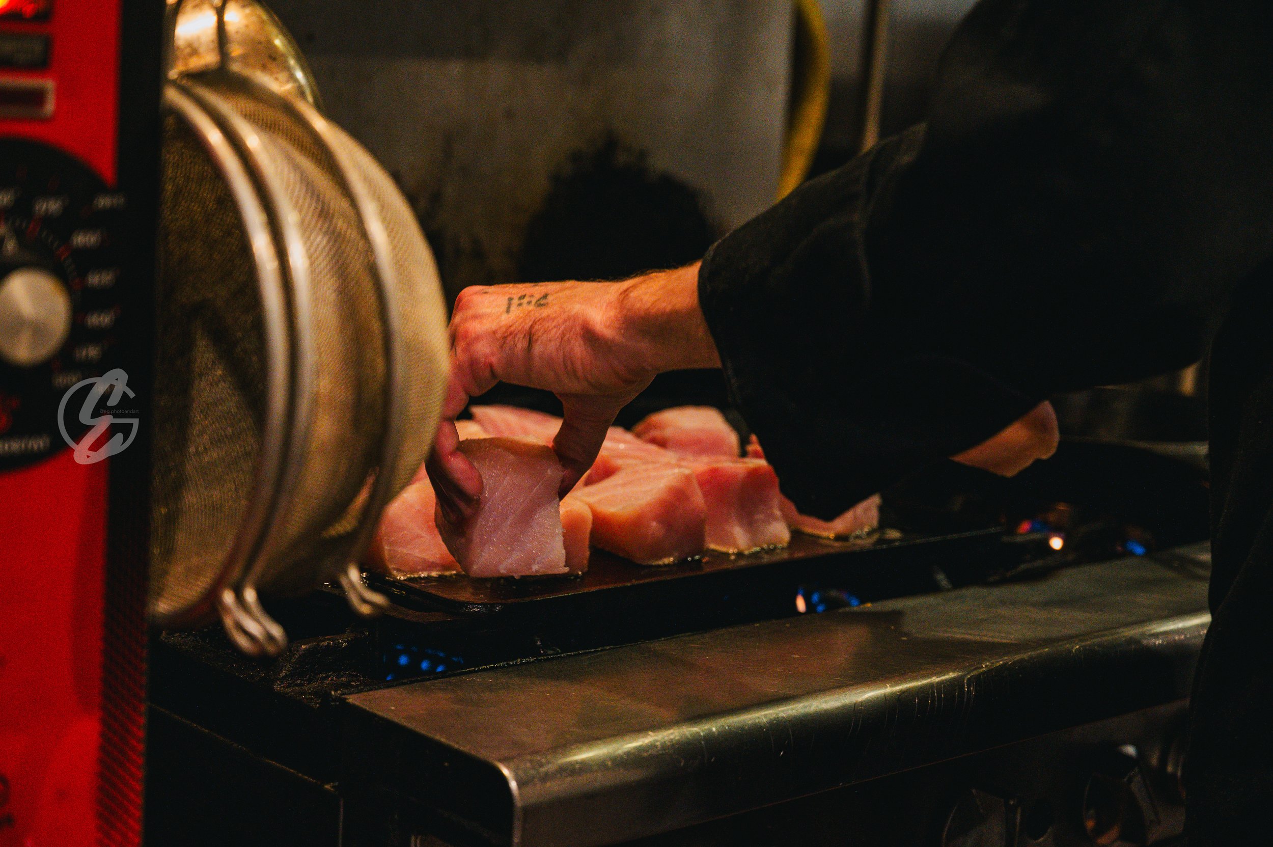 Person cooking pork chops on a stove with blue flames.