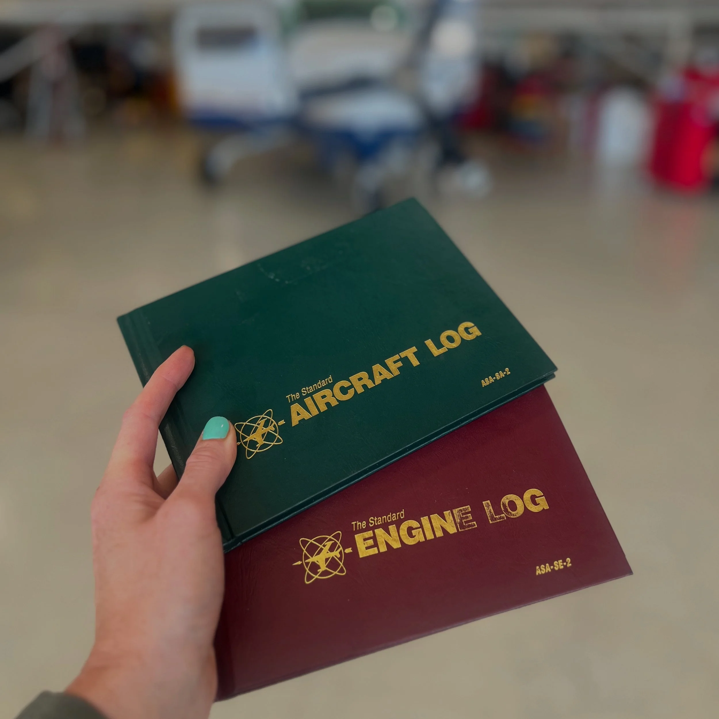 A person holding a green book titled 'The Standard Aircraft Engine' in their left hand, with a blurred classroom or library setting in the background.