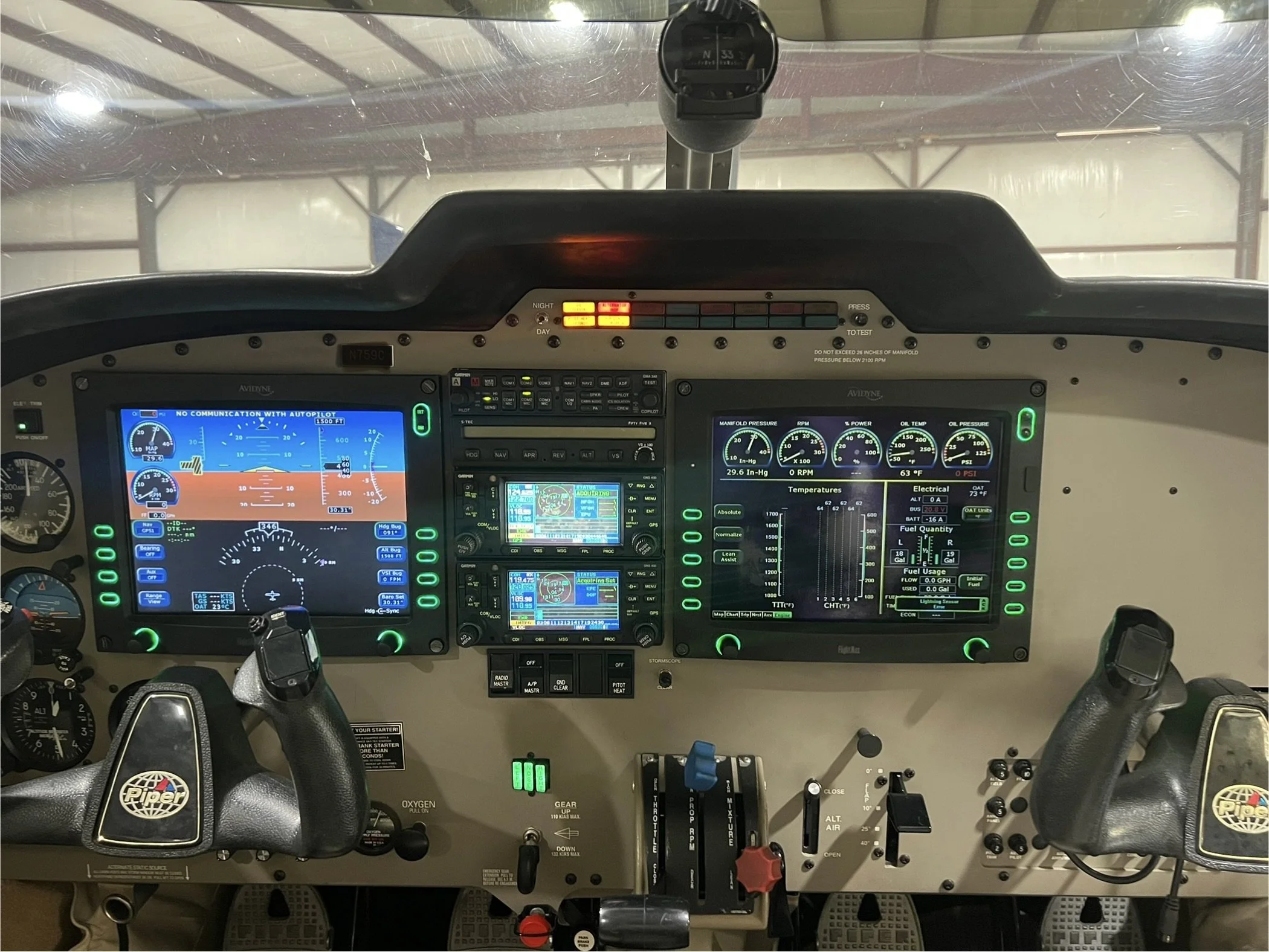 View of airplane cockpit instruments and controls, including digital screens, gauges, switches, and throttle levers.