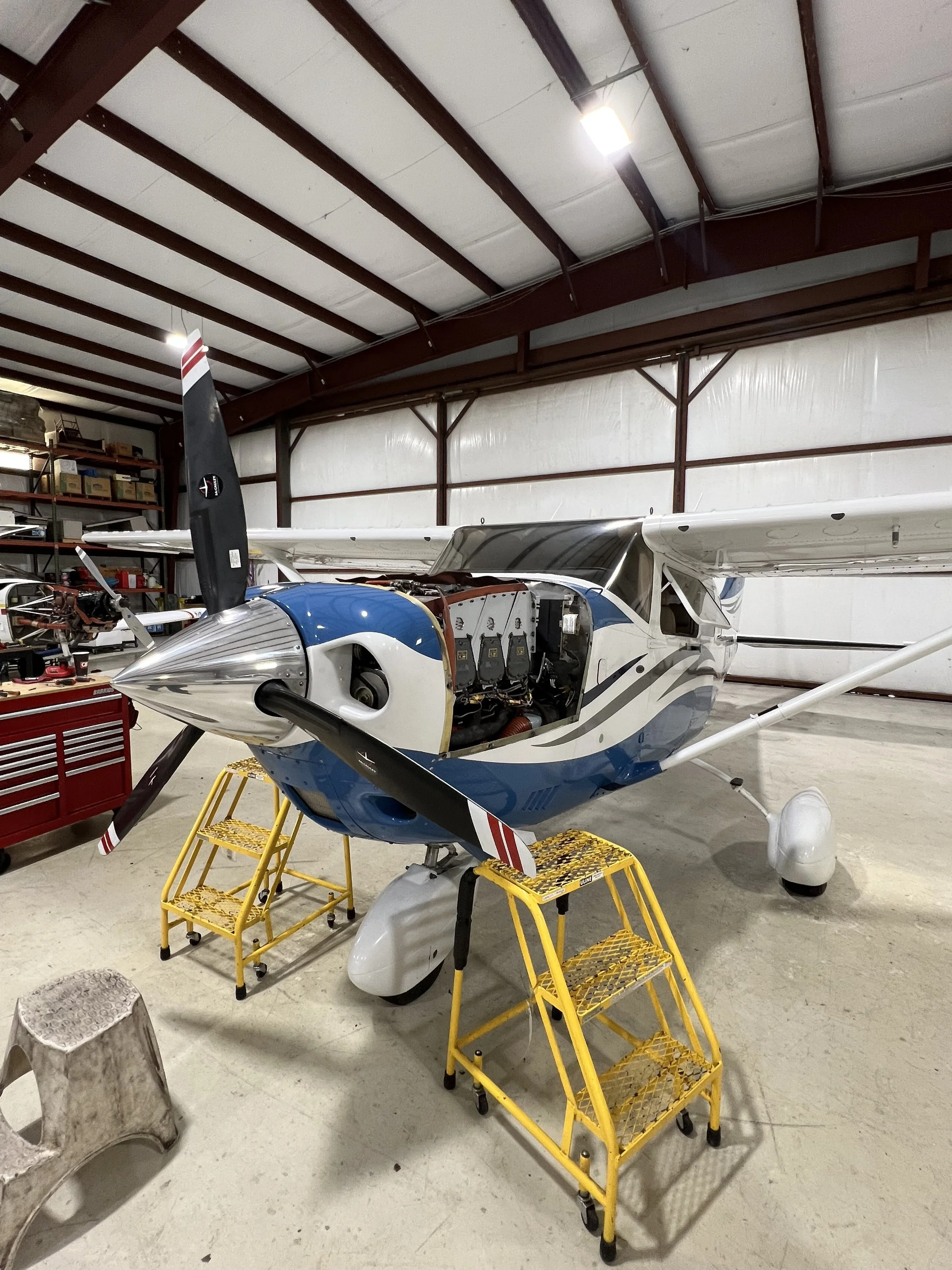 An airplane inside a hangar with four yellow rolling stairs set up around it for maintenance or repair.