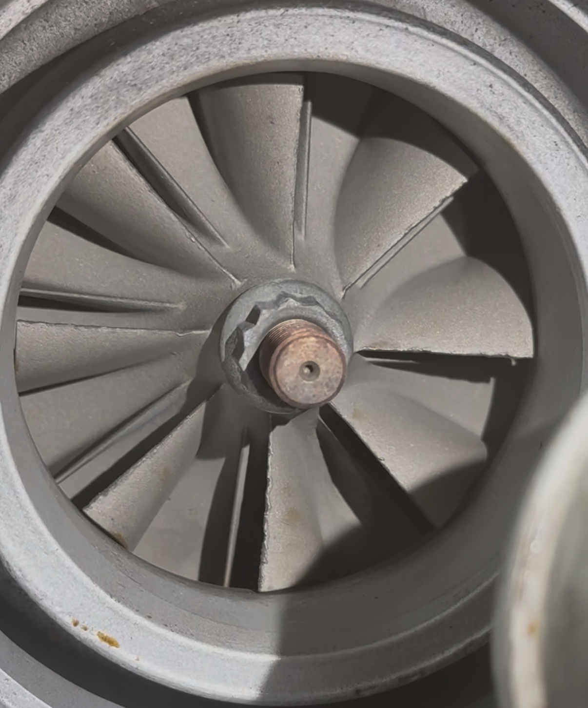 A close-up view of a metallic turbine or fan wheel with multiple blades and a central rusted bolt.