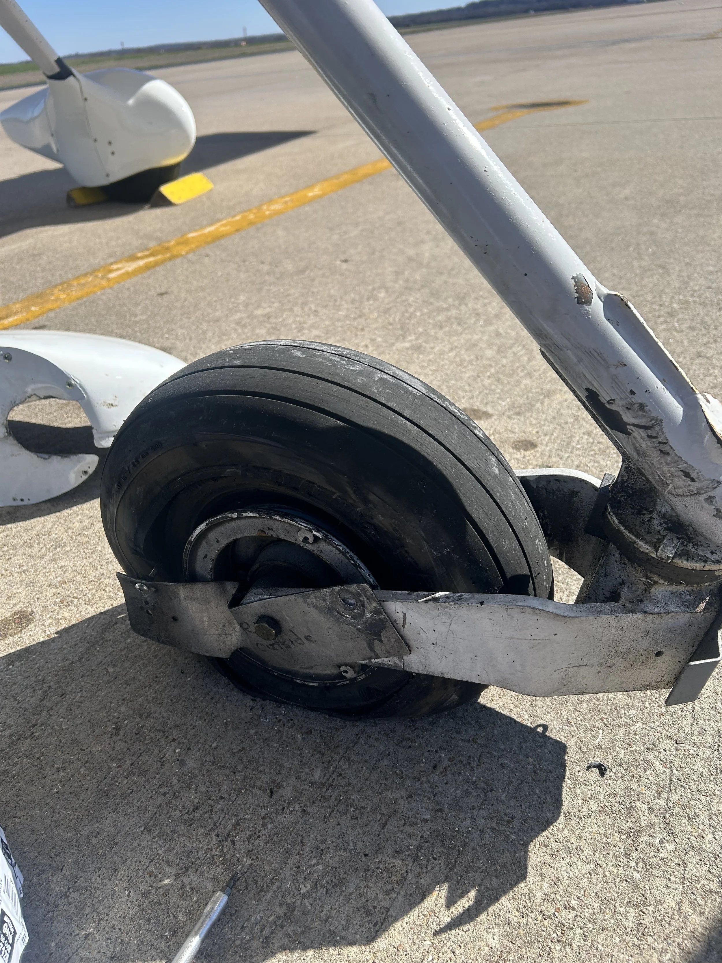 Close-up of an aircraft landing gear wheel and strut on an airport tarmac, with repair tools nearby.