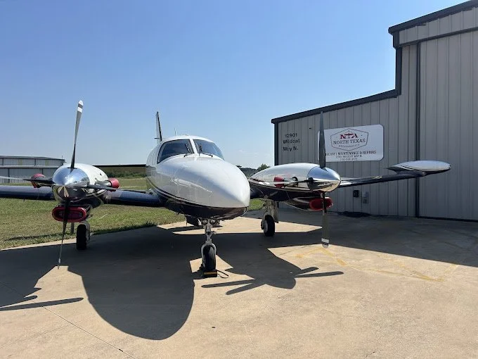 Small twin-engine airplane parked on the tarmac outside a hangar, with a sign indicating North Texas and Cessna.