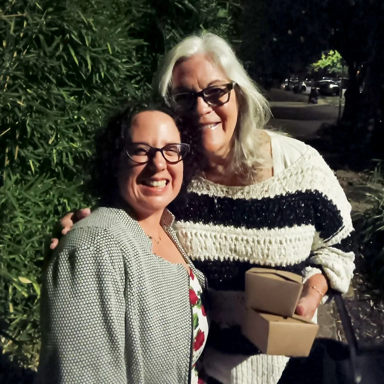 Two women stand with their arms around each other, smiling.