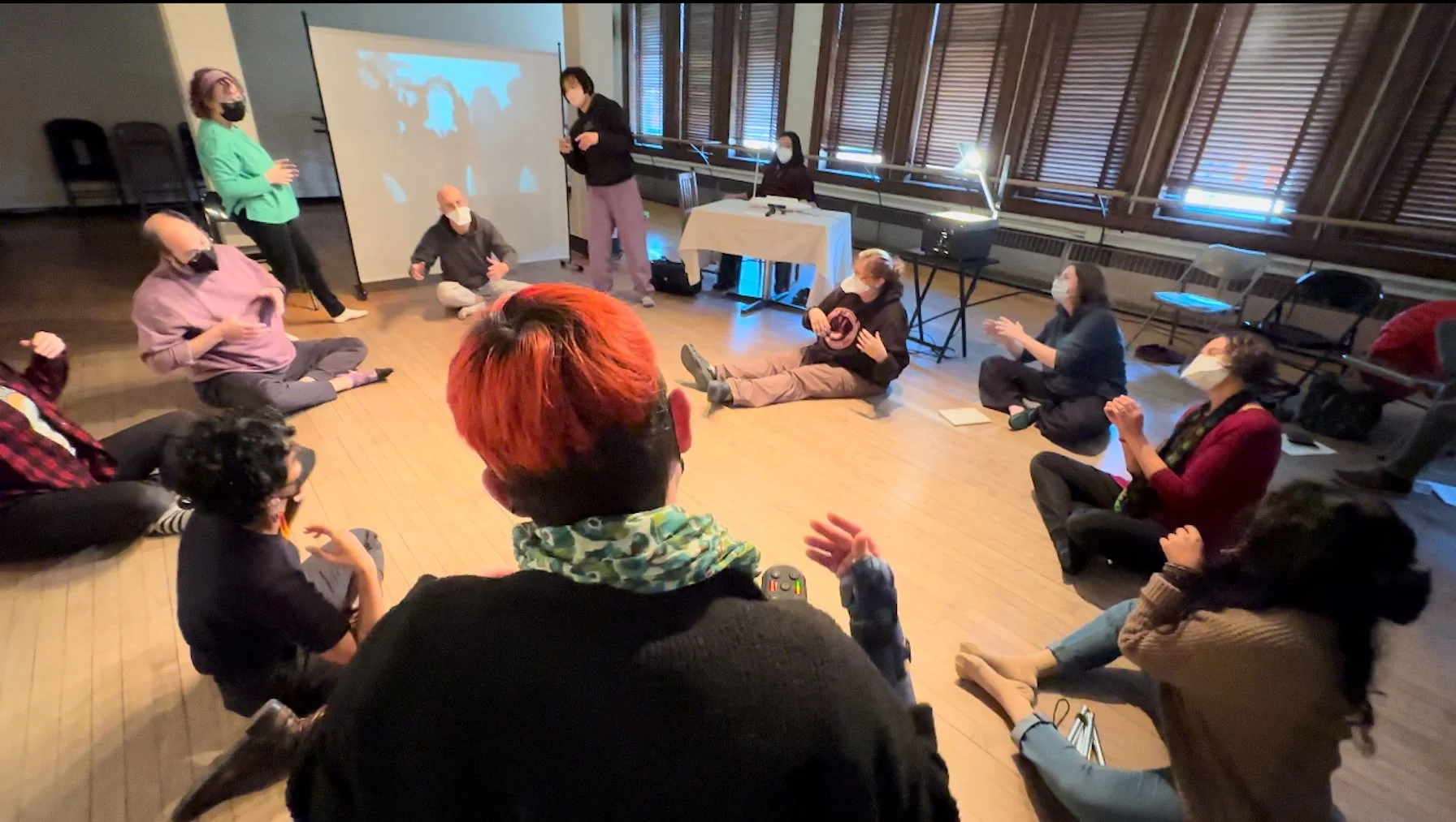 People sit and stand in a circle at a mad moves workshop.