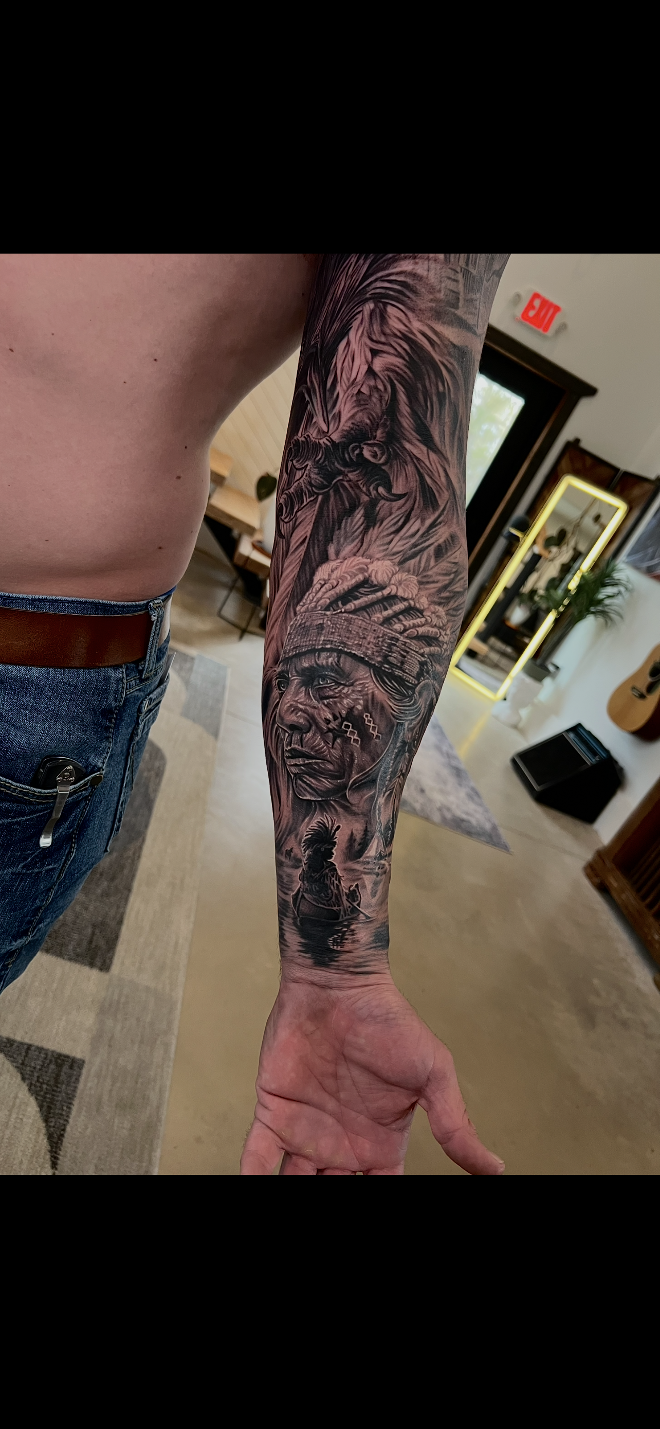 Black and gray tattoo sleeve featuring a Native American woman's portrait, a native canoe, a wolf, and a bird, on a person's arm and forearm.