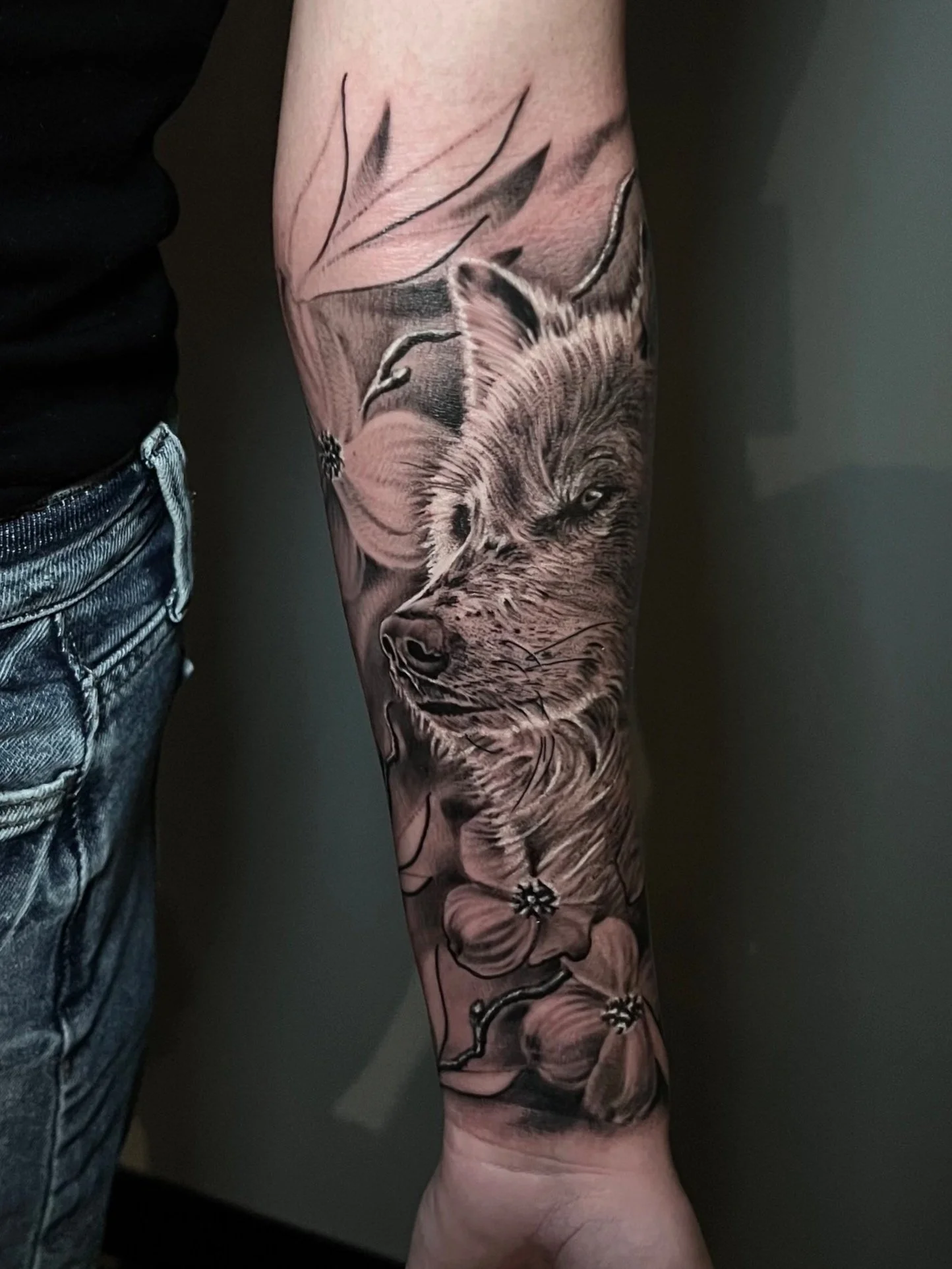 Black and gray tattoo of a wolf's face surrounded by flowers on a person's arm.