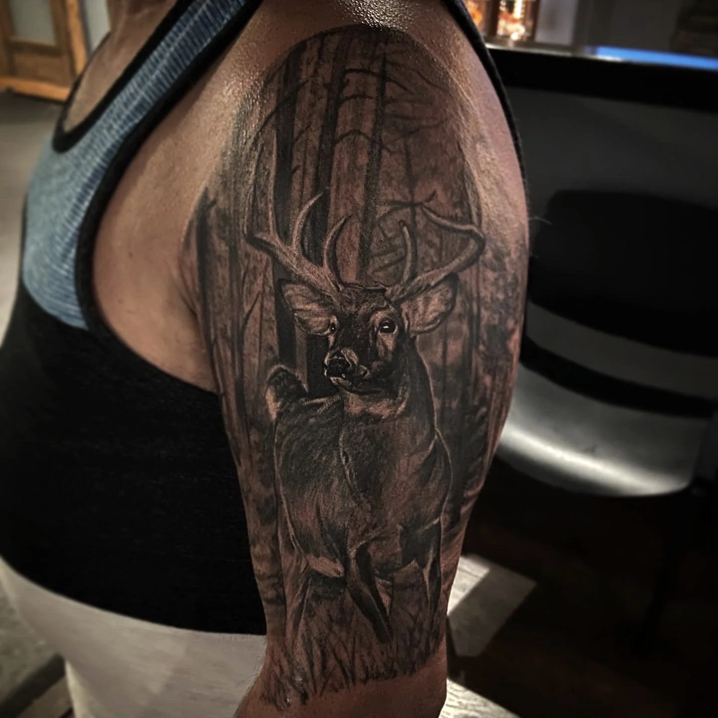 Tattoo of a deer with large antlers in a forest scene.