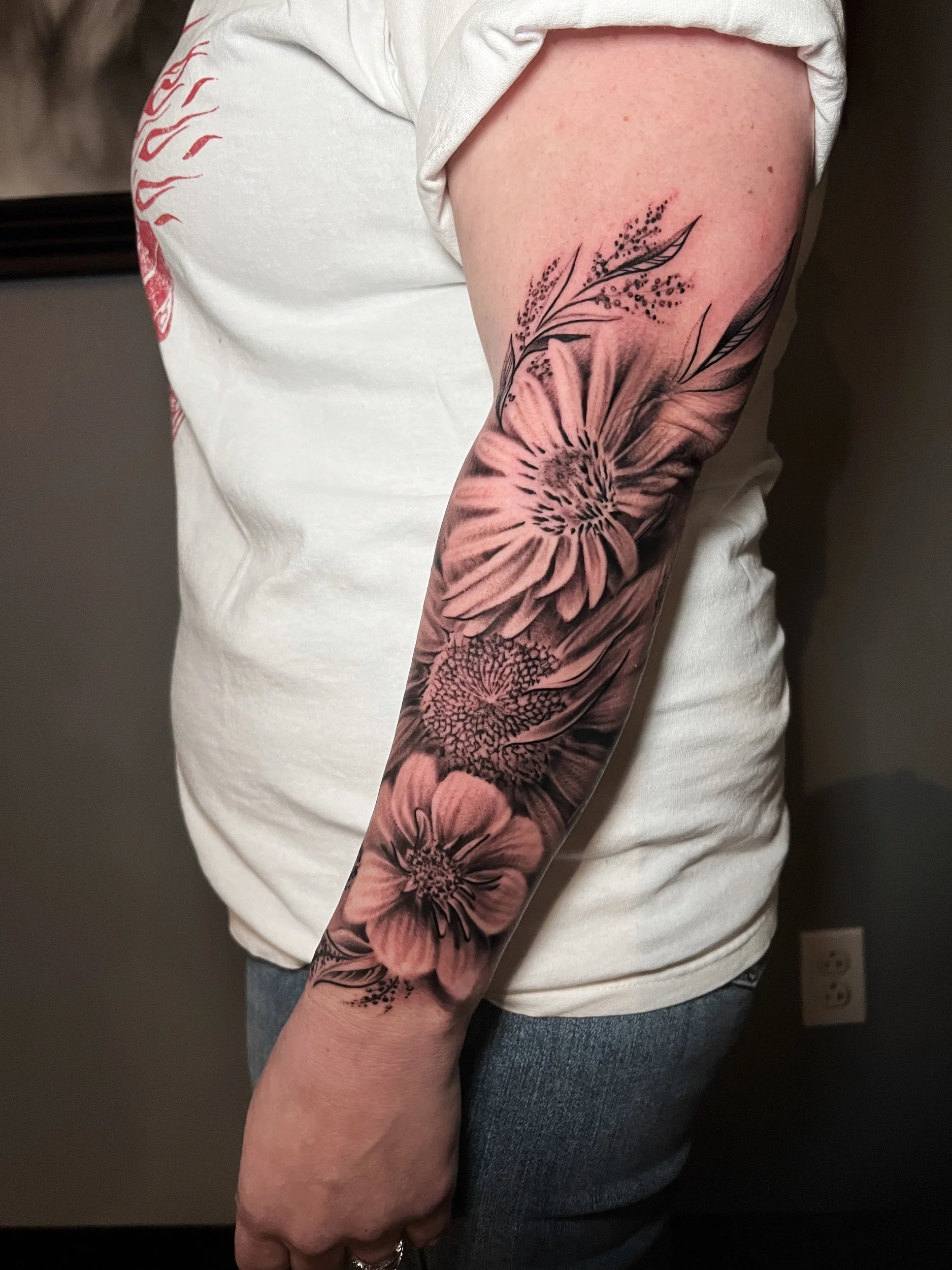 A person's arm with a detailed black and gray floral tattoo featuring large flowers and leaves.