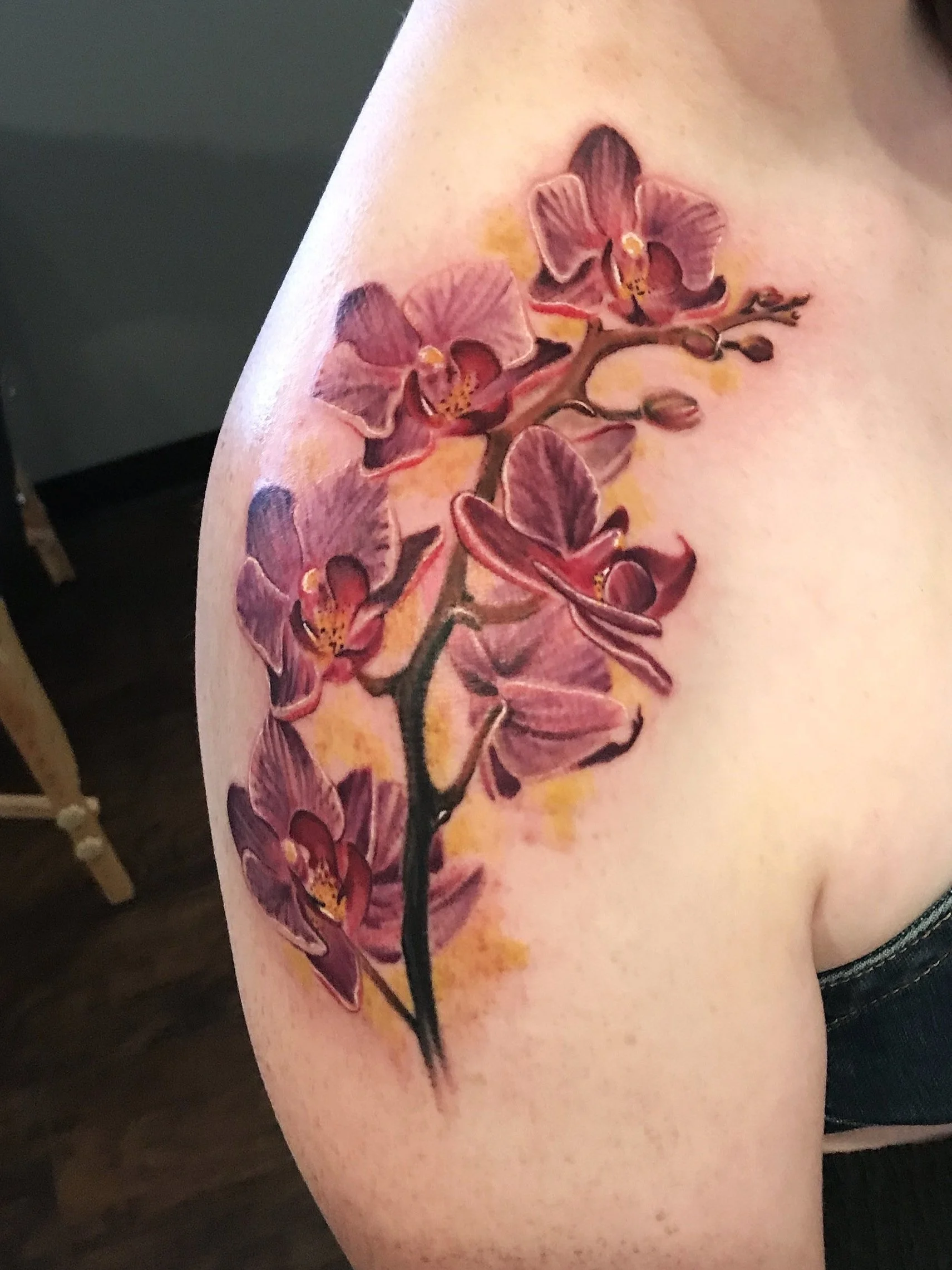 Colorful tattoo of pink and purple orchids with a yellow background on a person's upper arm.