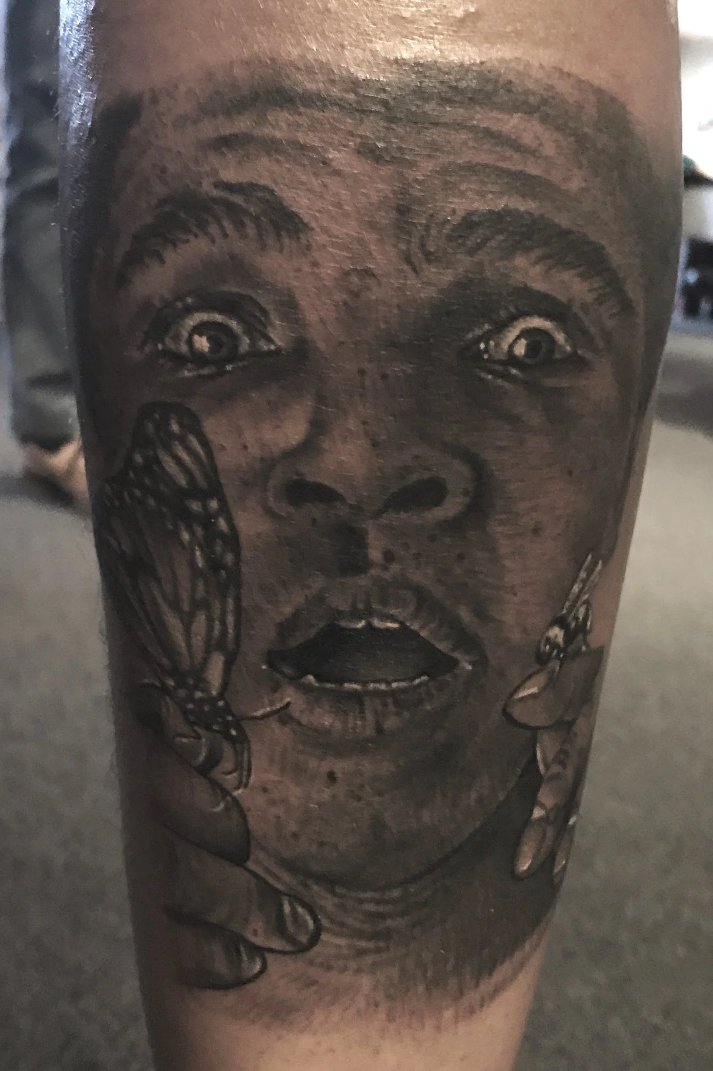 Close-up of a tattoo depicting a surprised face with wide eyes and open mouth, with two butterflies resting on the person's hand.