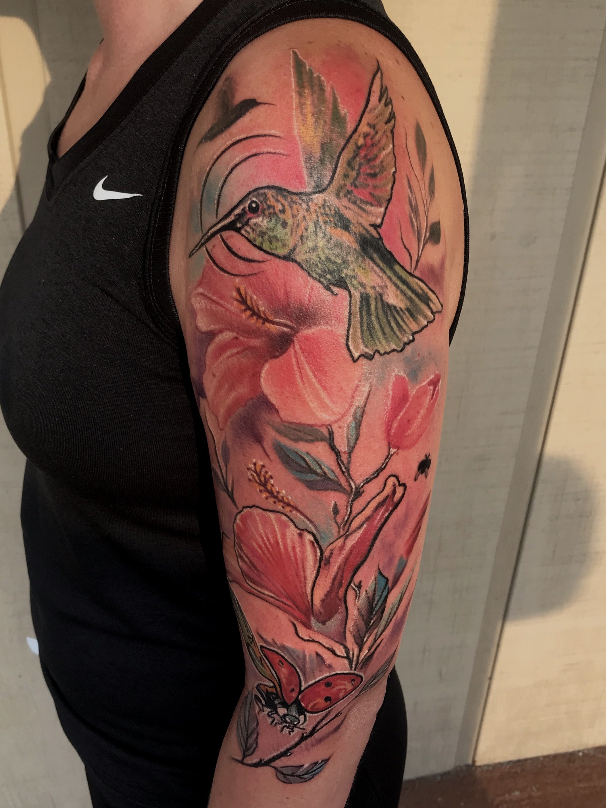 Colorful tattoo of a hummingbird, butterfly, and floral elements on person's upper arm.