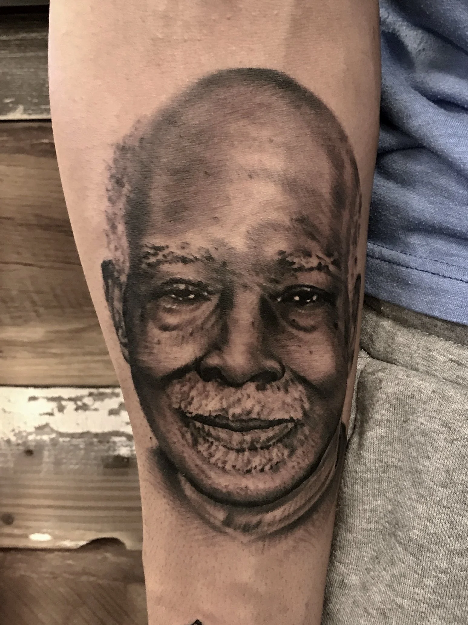 Black and gray realistic tattoo of an elderly man’s face with a broad smile on the arm.