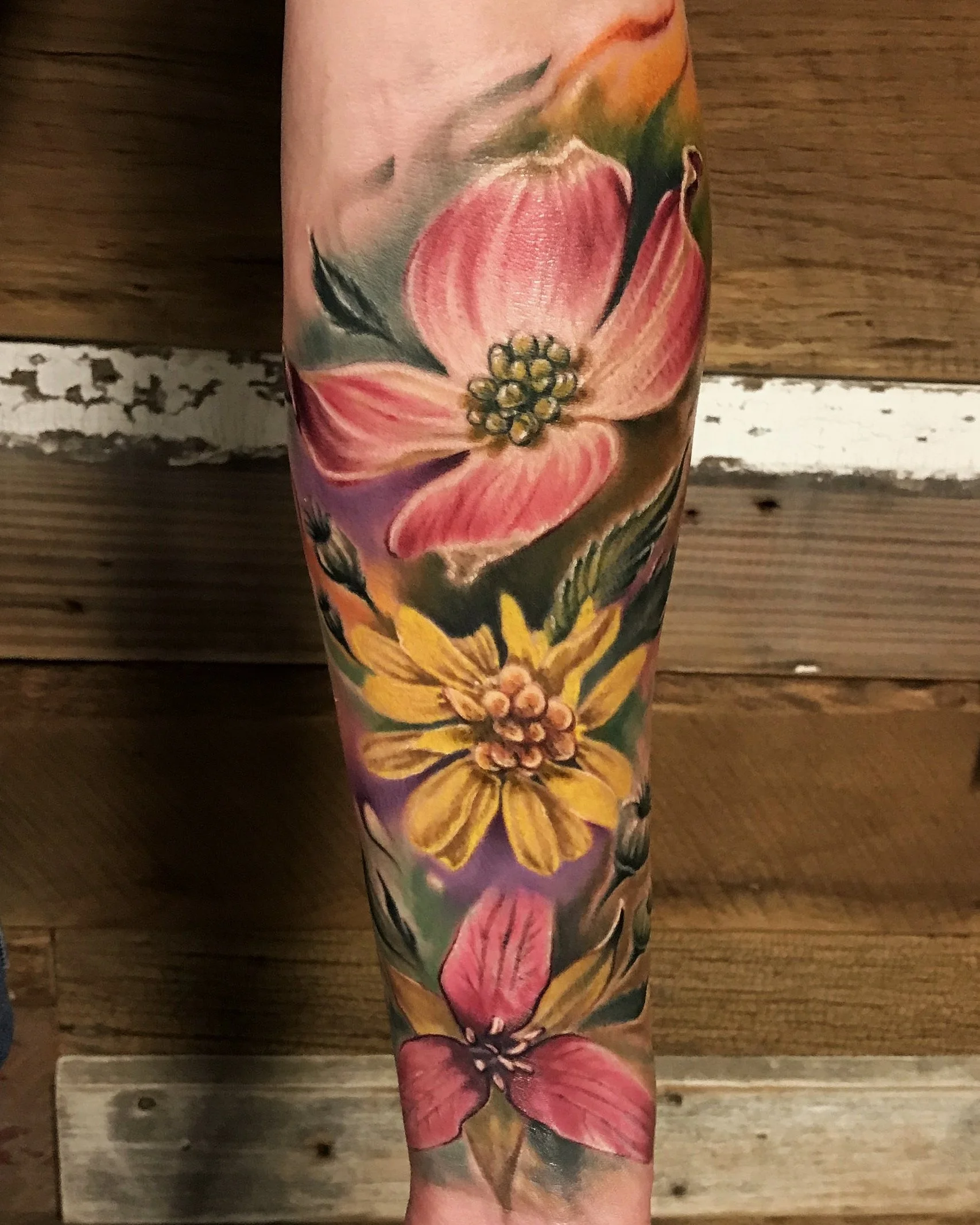 Colorful floral tattoo sleeve featuring pink, yellow, and purple flowers on a person's arm.