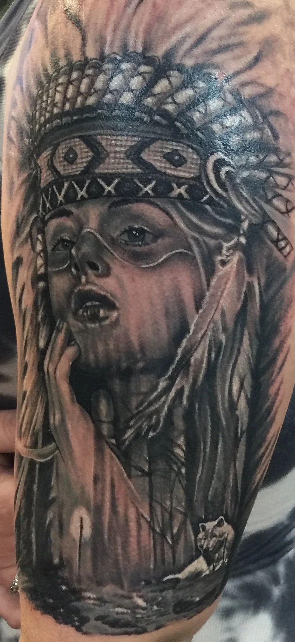 Black and gray tattoo of a woman with tribal face paint and headdress, hand on chin, with a small animal like a fox or dog at her side.