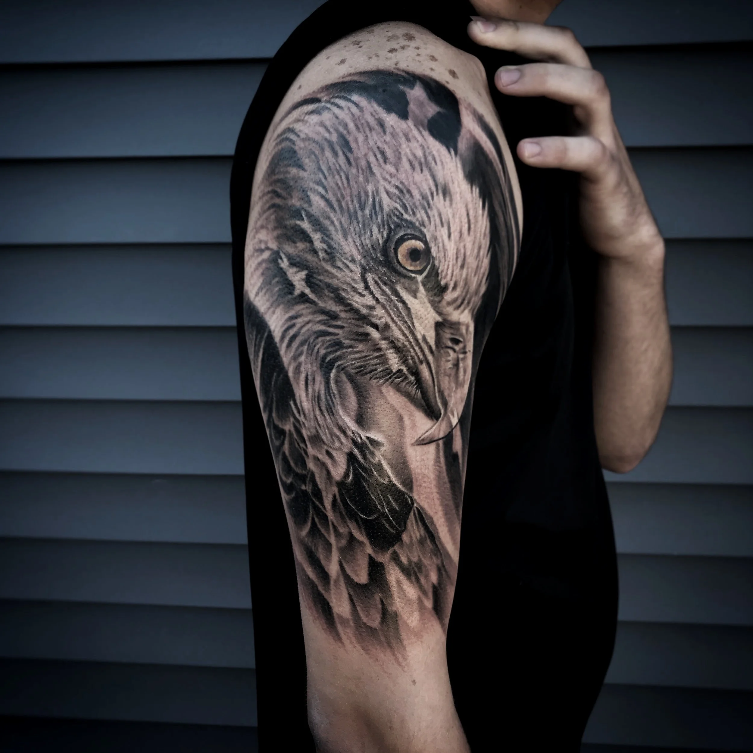 Close-up of a person's upper arm with a detailed black and gray tattoo of an eagle's head.