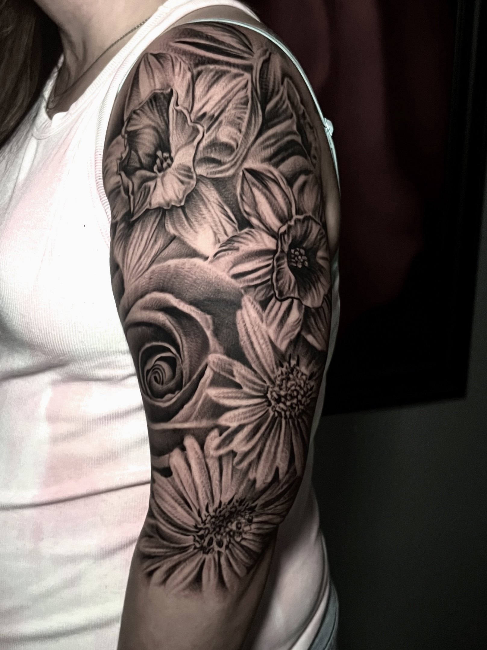 Black and gray floral tattoo on person's upper arm, featuring various flowers including roses and daisies.