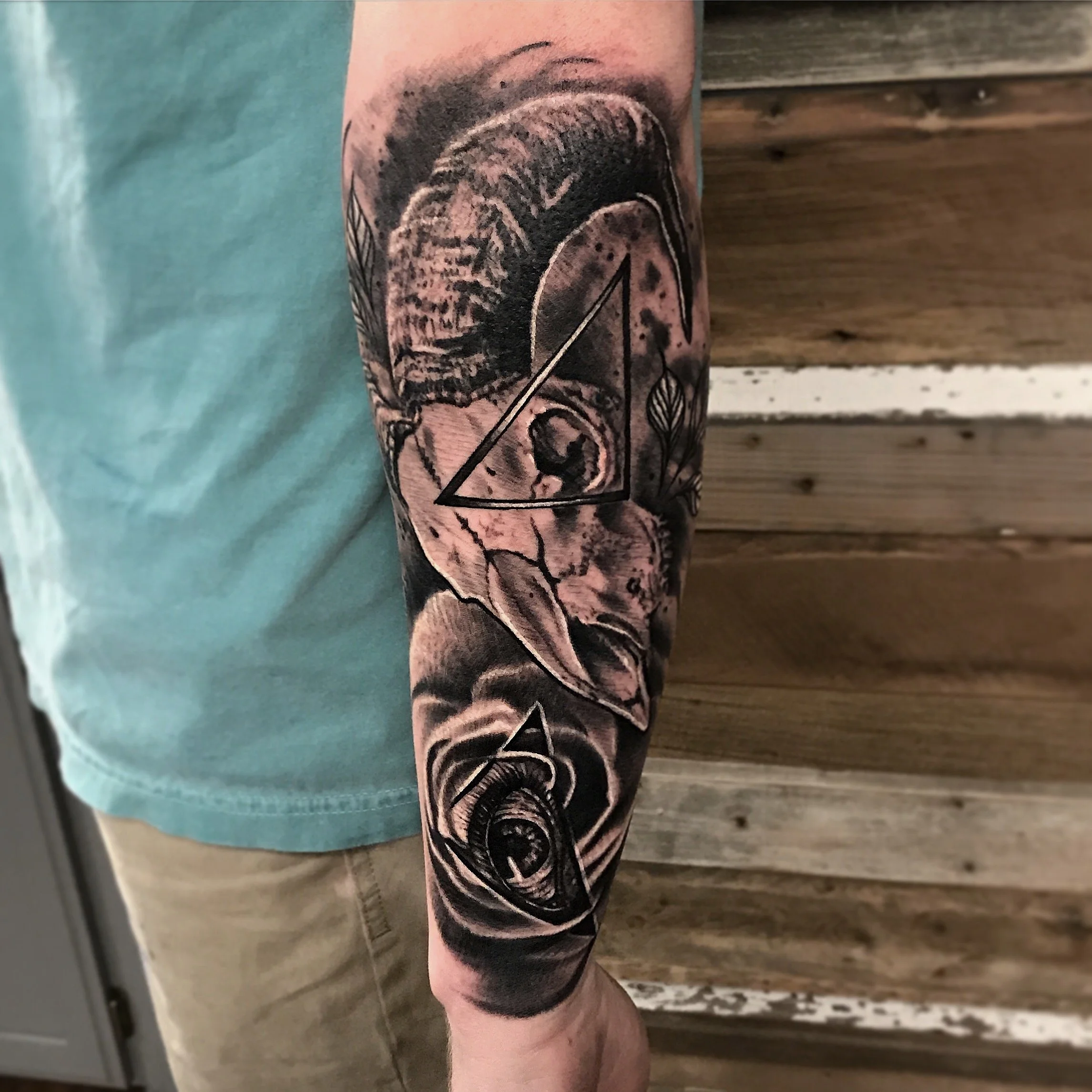 Black and gray tattoo of a portrait with geometric elements on a person's arm, featuring a bear with leaves and a spiral eye.