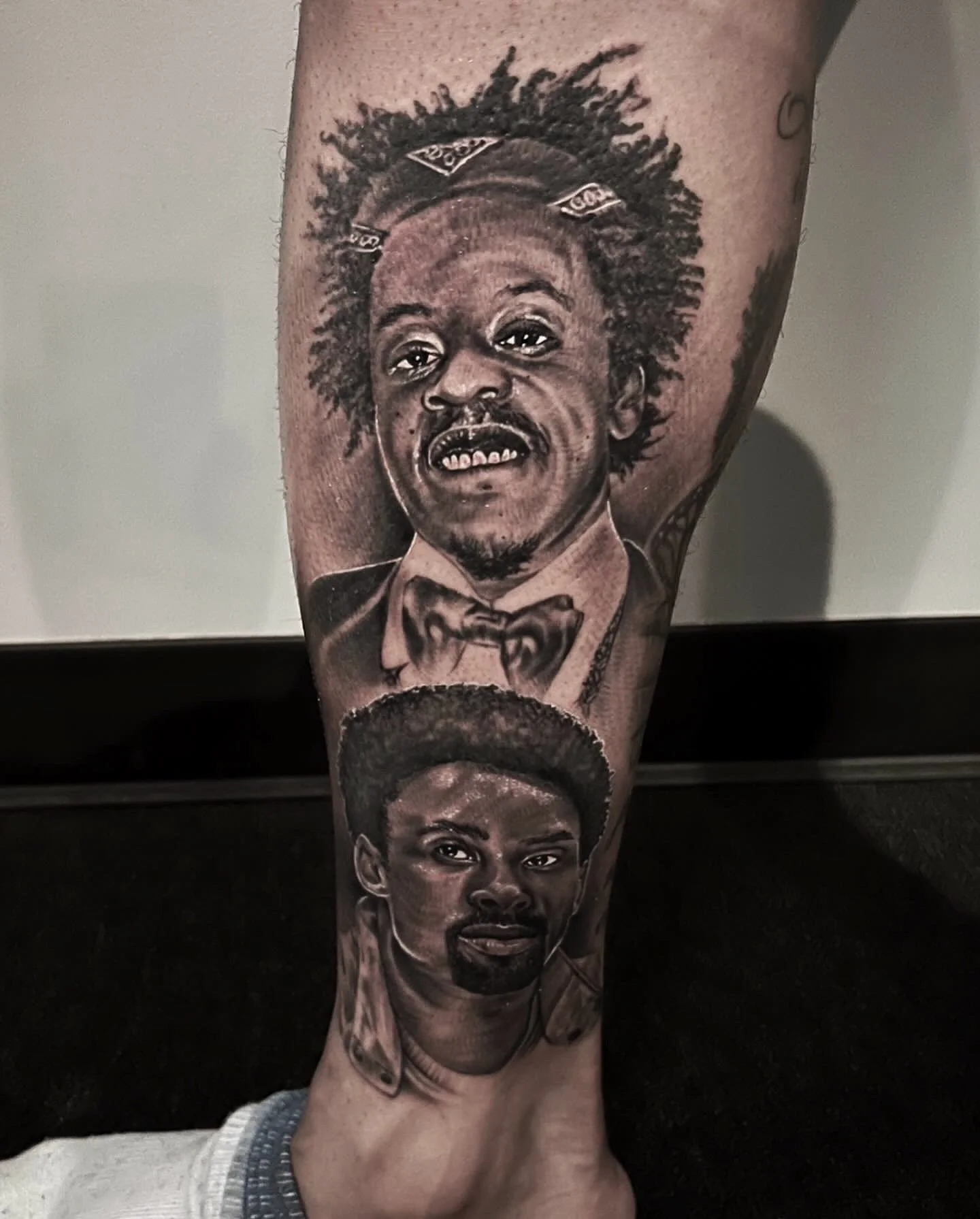 Black and gray tattoo of two men's faces on a person's leg, with detailed shading and realistic style.