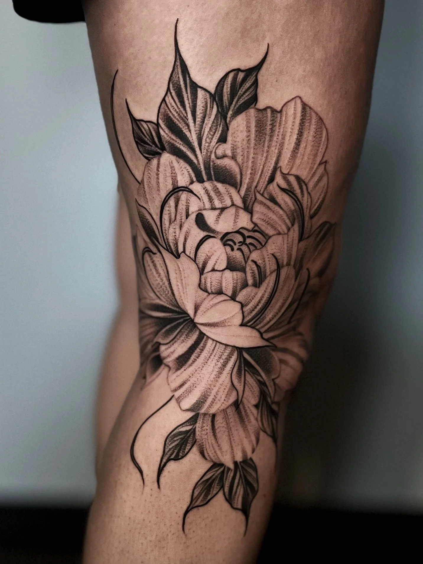 Black and gray floral tattoo on person's arm, featuring a large flower with detailed petals and leaves.