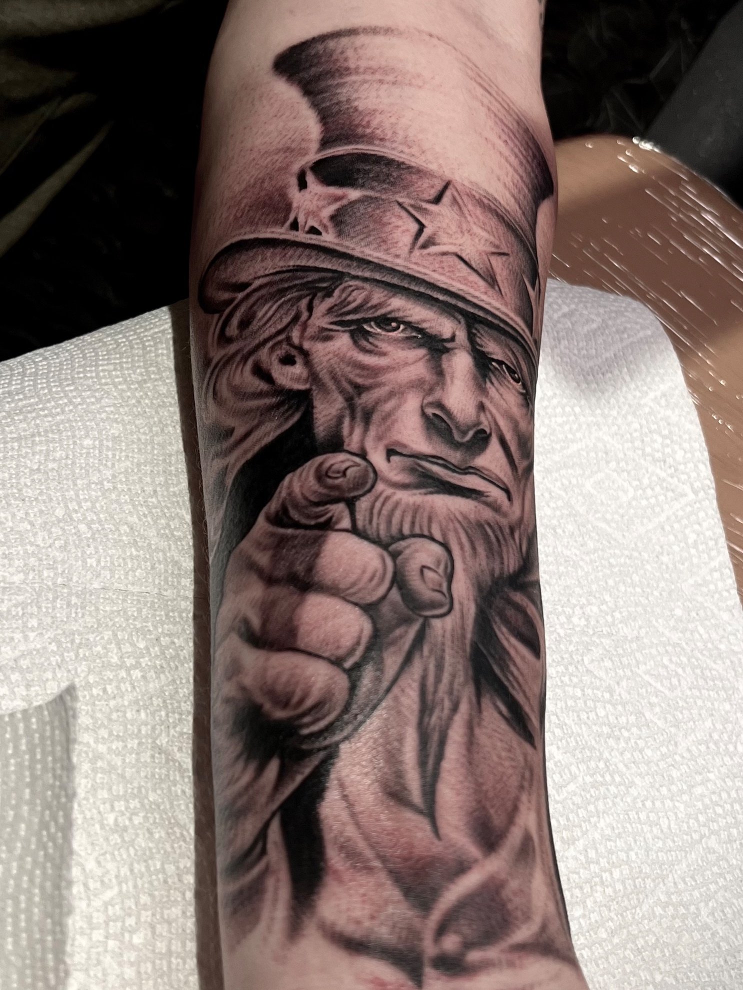 Black and gray tattoo of a U.S. soldier with a serious expression, pointing directly at the viewer, wearing a helmet with a star emblem.