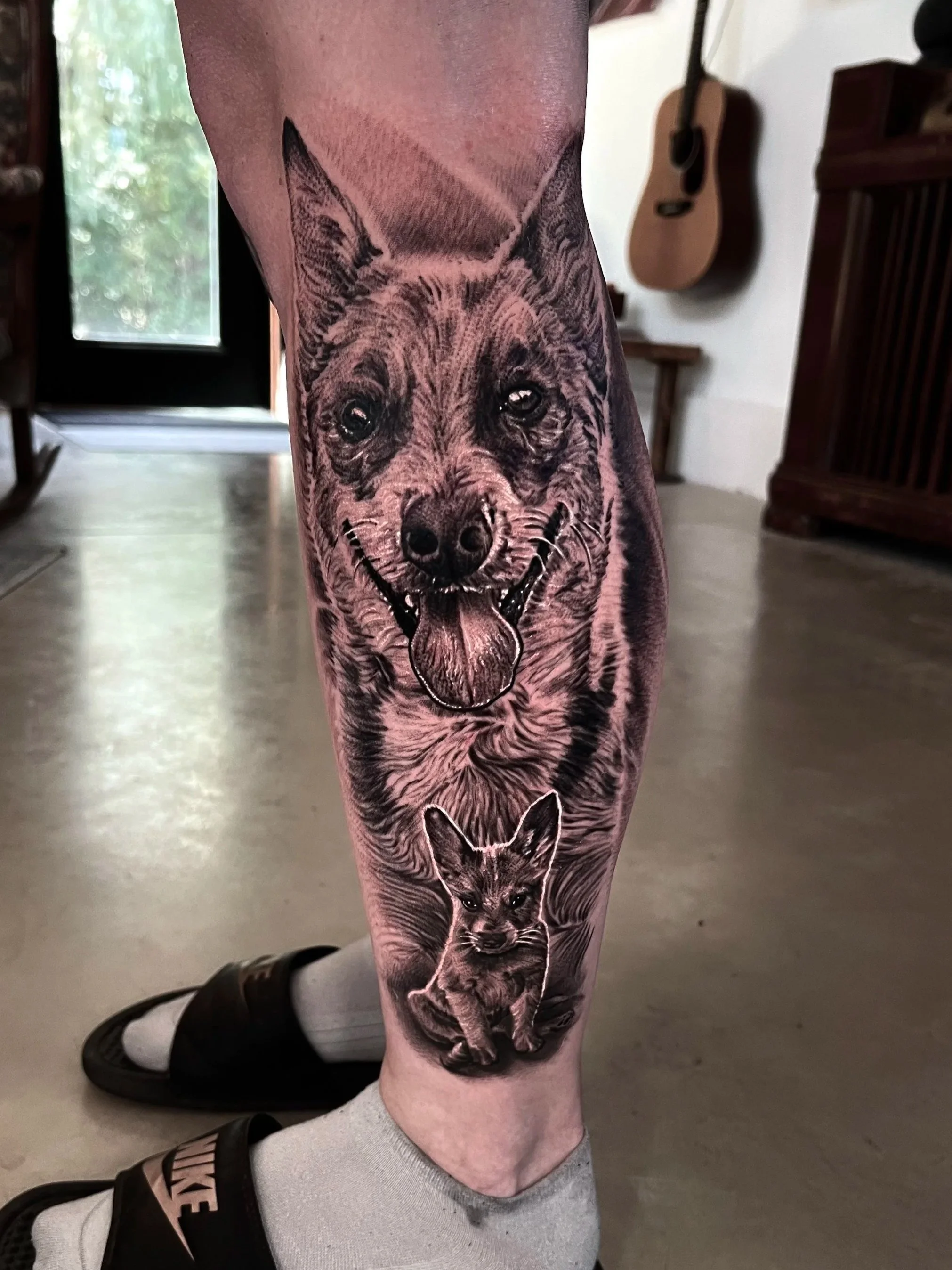 Tattoo of a dog and a cat on person's leg, with a large dog face and a smaller cat face beneath.