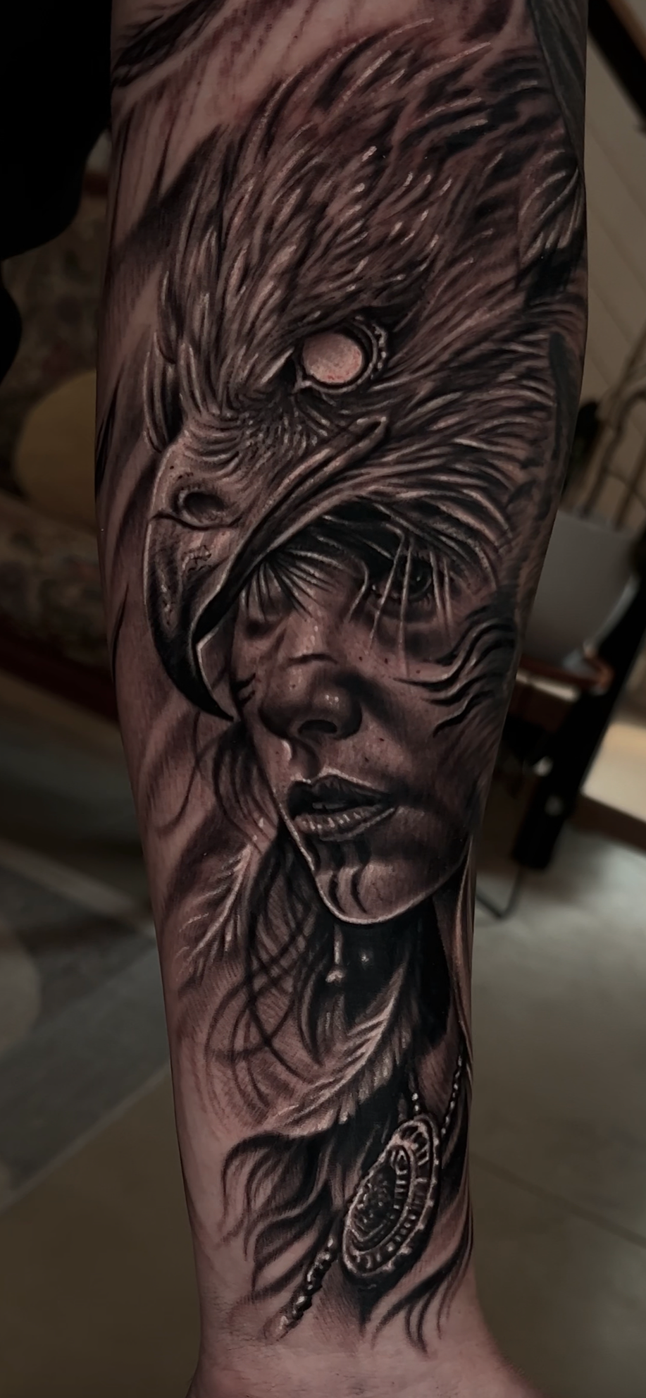 A realistic black and gray tattoo of a woman's face with long flowing hair and a fierce wildcat face integrated into her head, with a detailed pendant hanging from her hair.