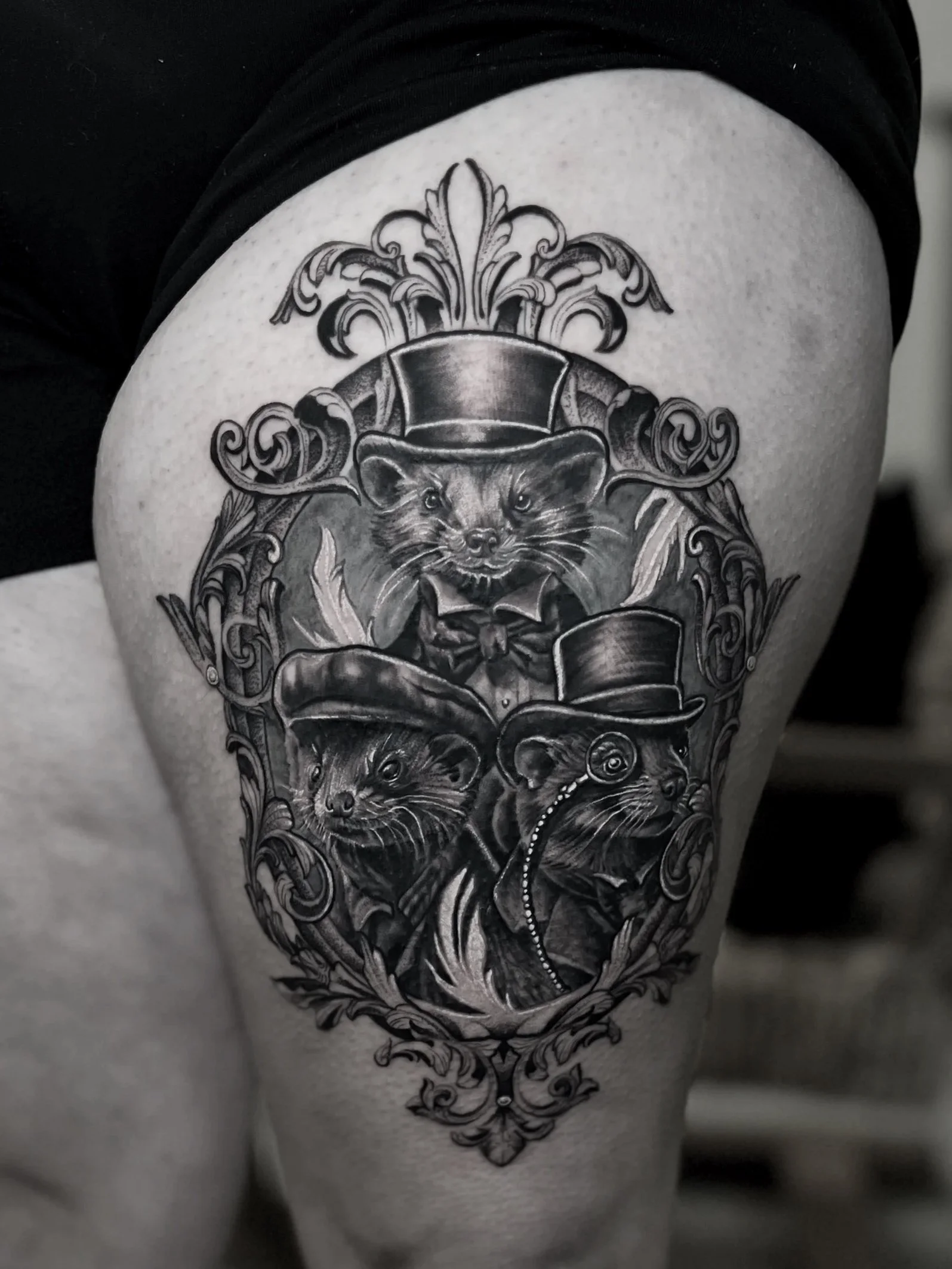Black and gray tattoo featuring three rats with Victorian style accessories, including hats, a monocle, and a ribbon, surrounded by ornate decorative elements.