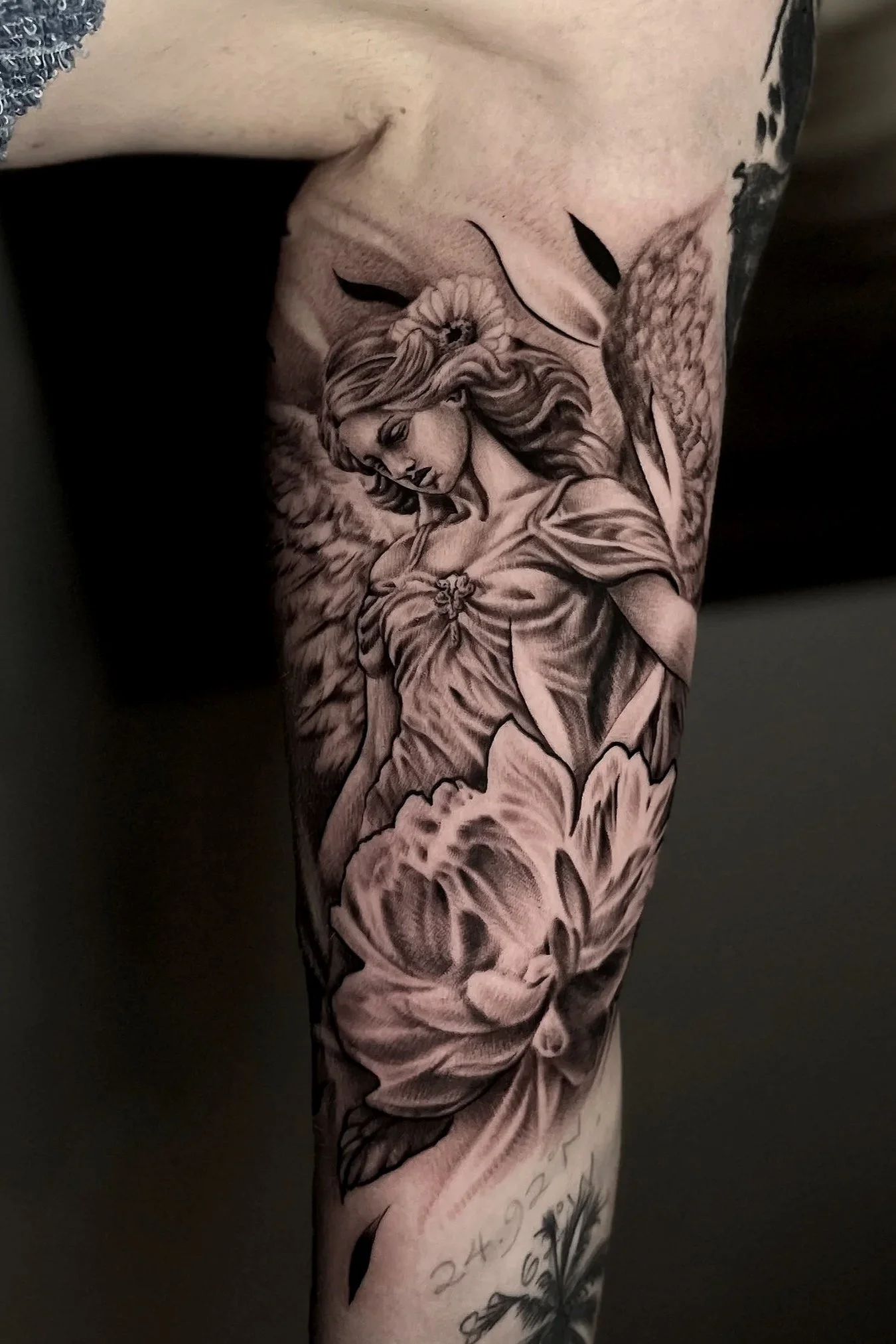 Black and gray tattoo of a woman with flowing hair surrounded by flowers, on a person's arm.