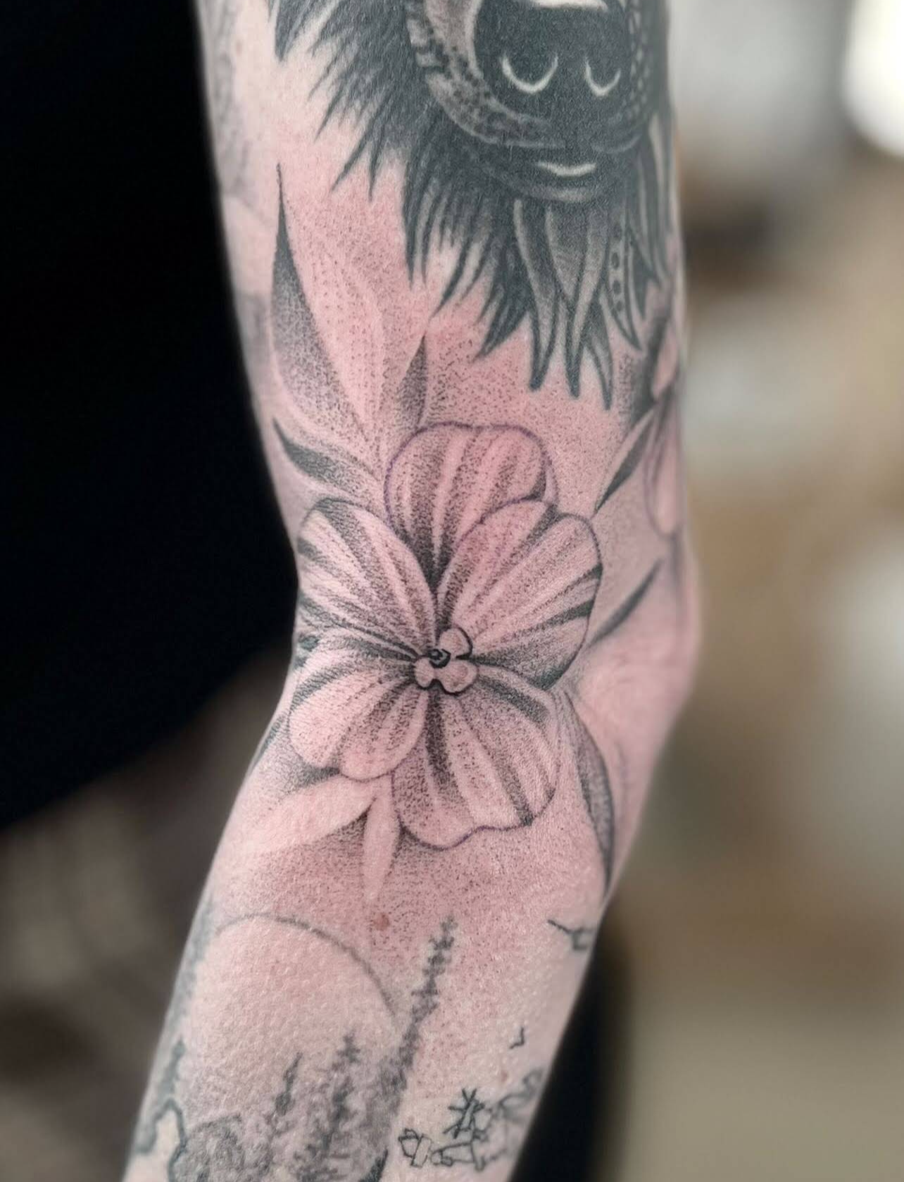 Close-up of a tattooed arm with floral and animal-themed designs in black and gray ink.