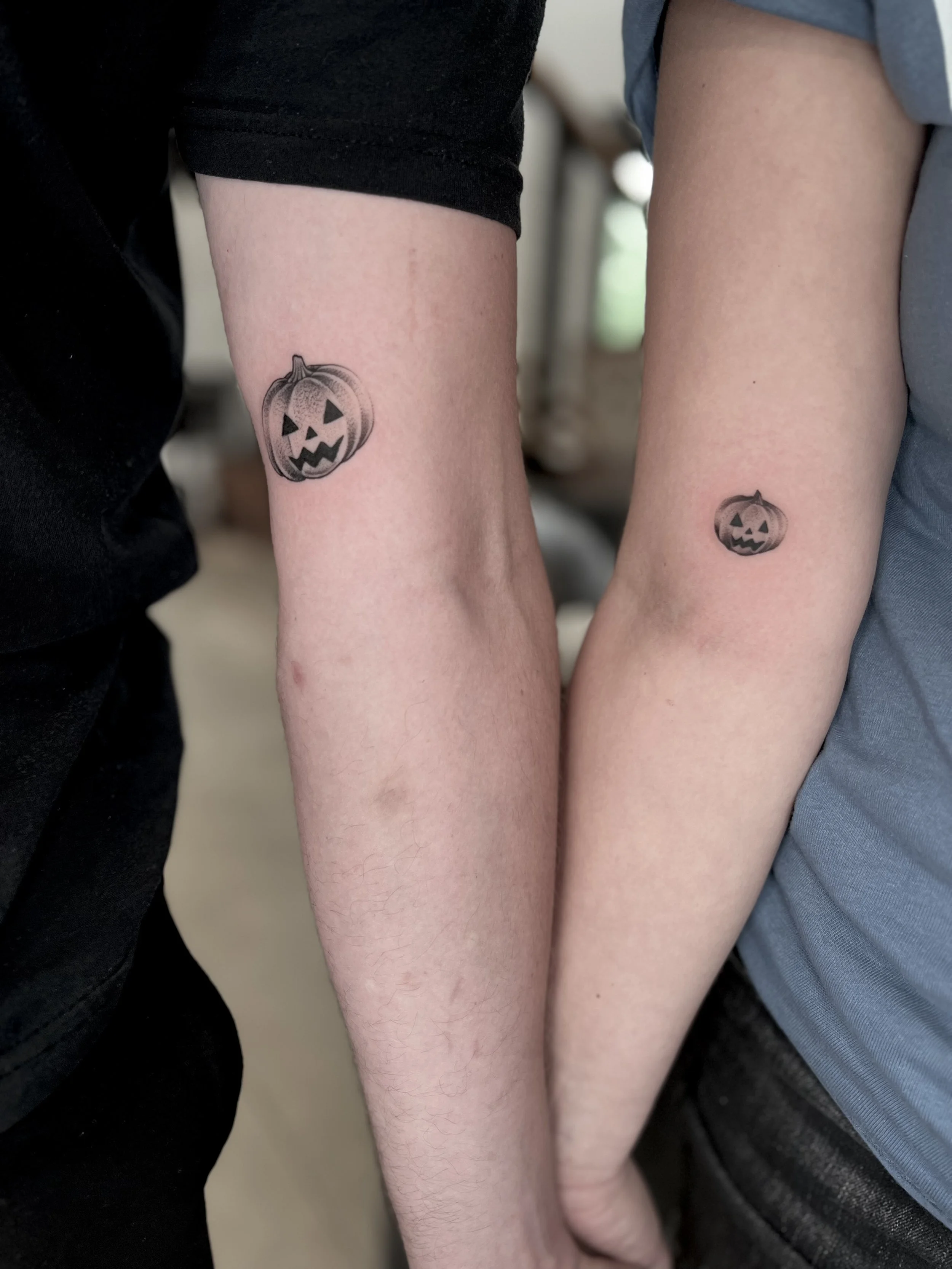 Two people's forearms with matching Halloween pumpkin tattoos.