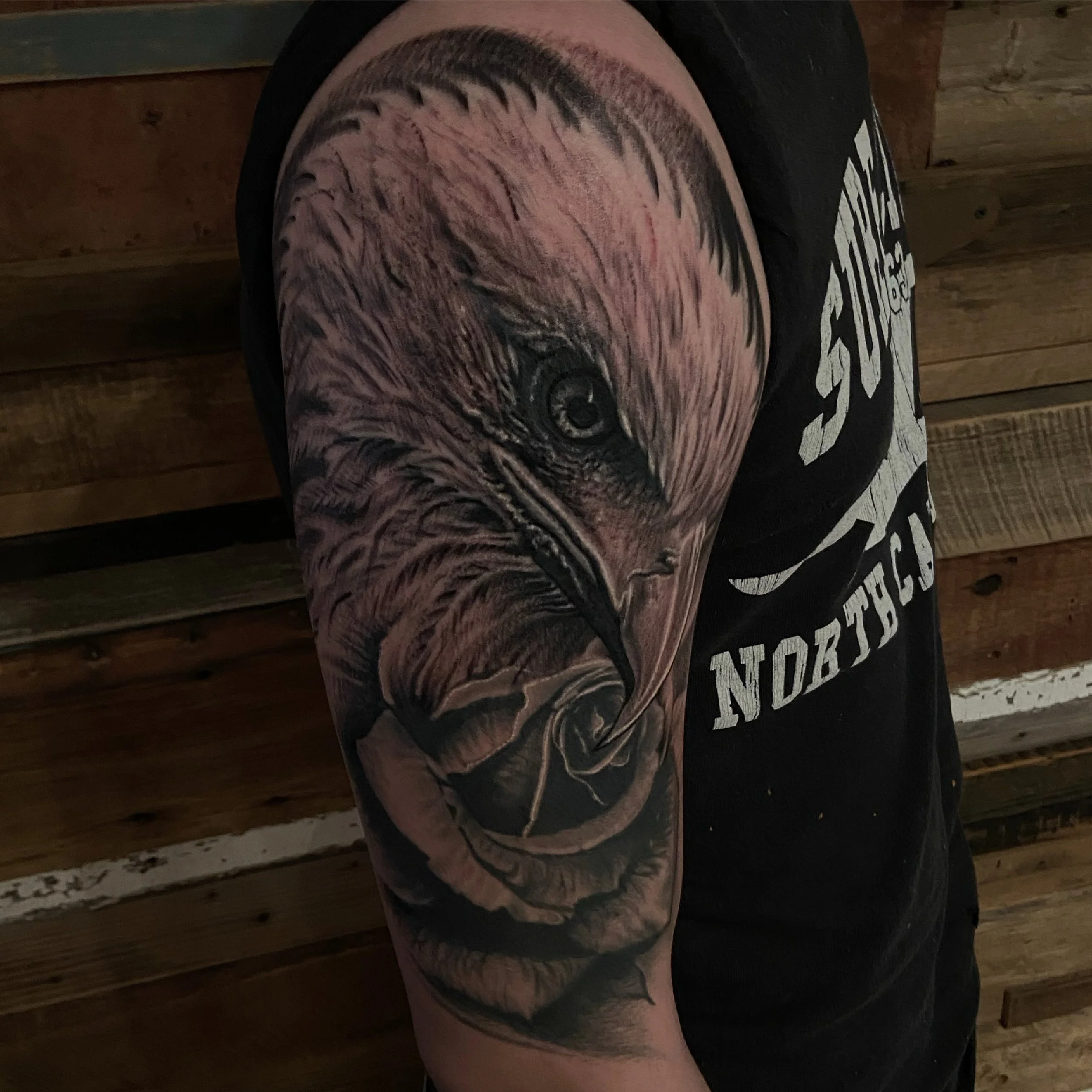 Tattoos of a detailed bald eagle head covering the upper arm.