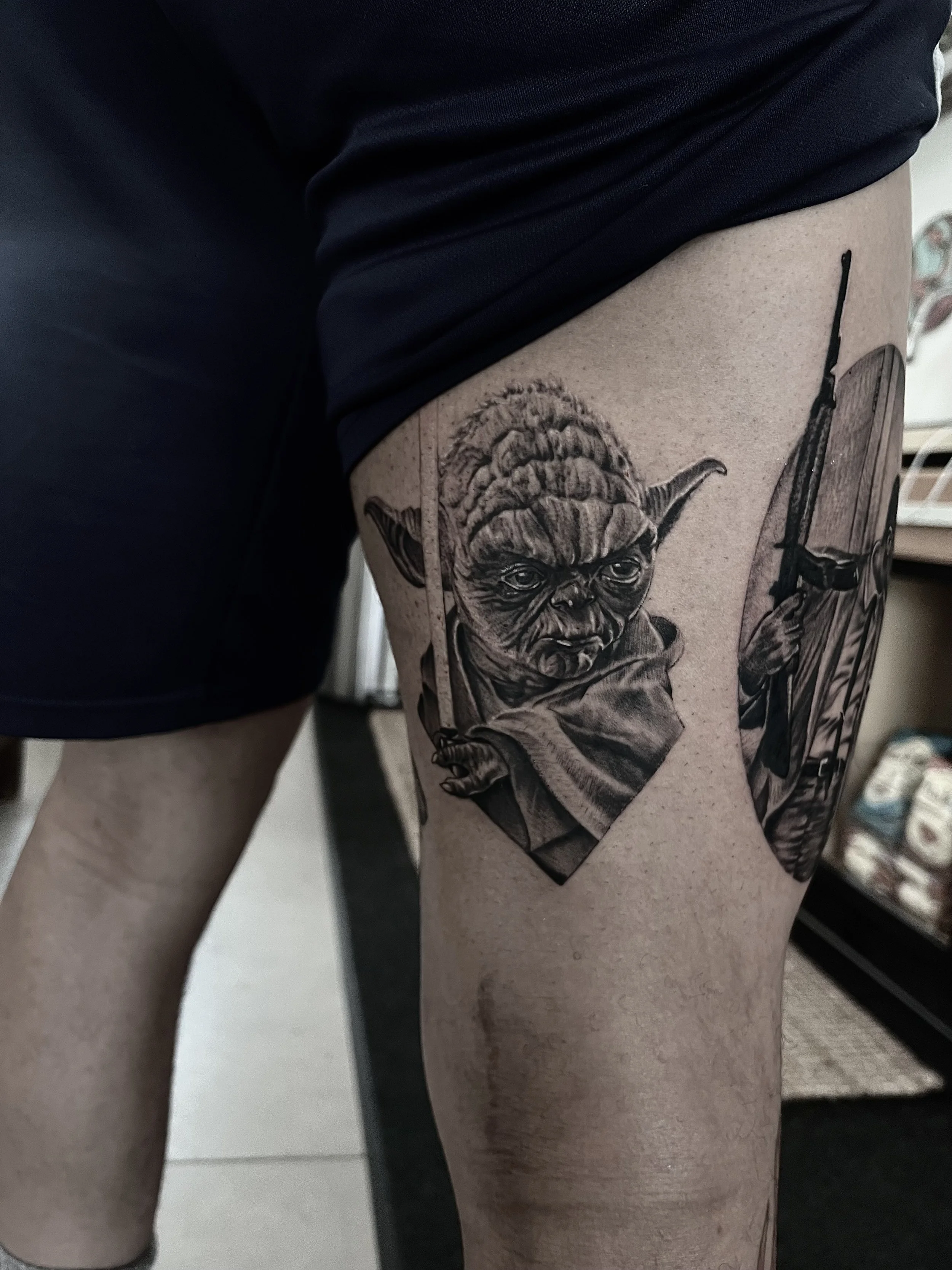 Tattoo of Yoda from Star Wars on a person's thigh, showing Yoda's face with two daggers crossed behind him.