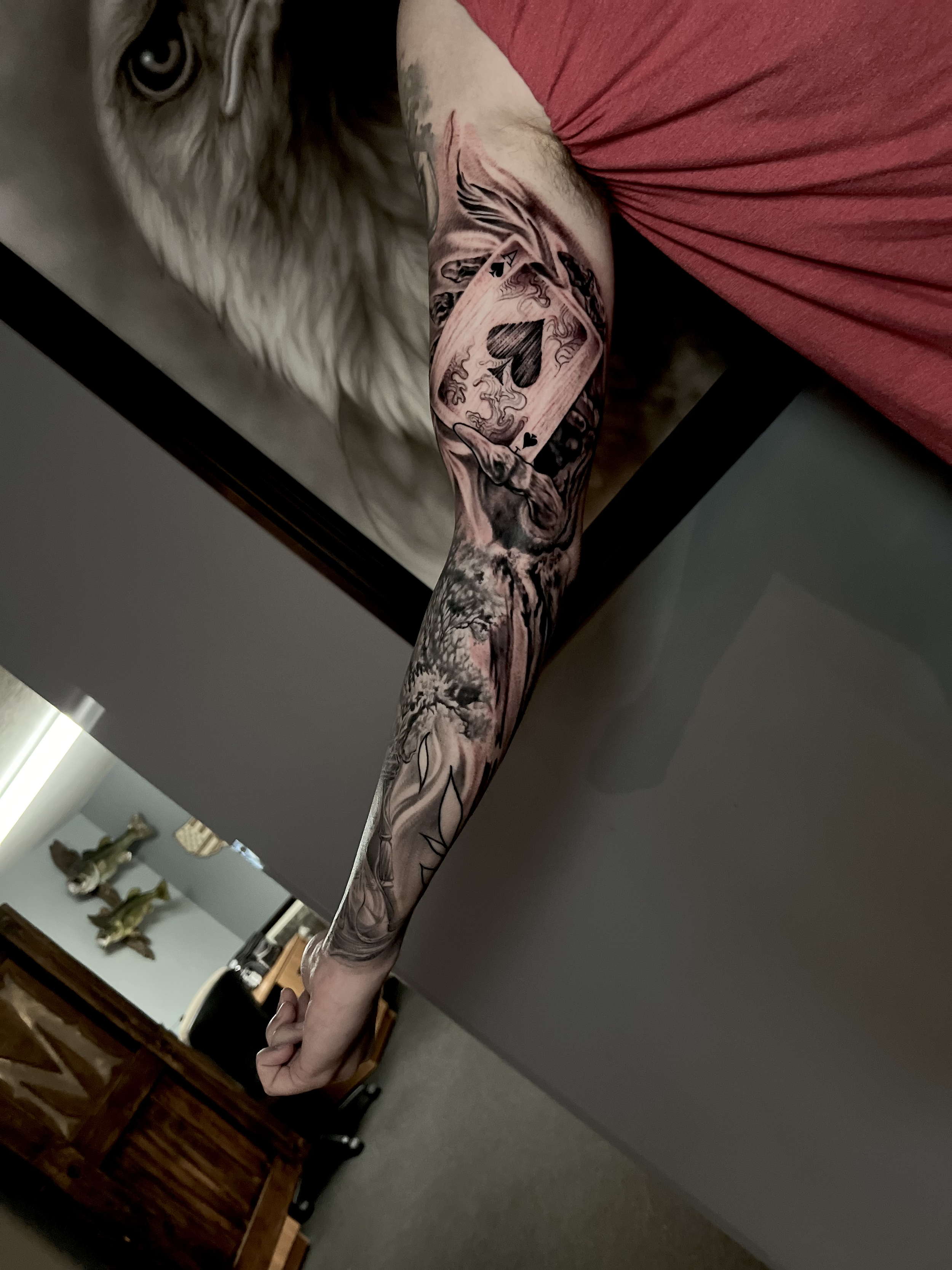 A person with a sleeve tattoo extending from shoulder to wrist, featuring a playing card, while lying on a bed with a dog nearby.