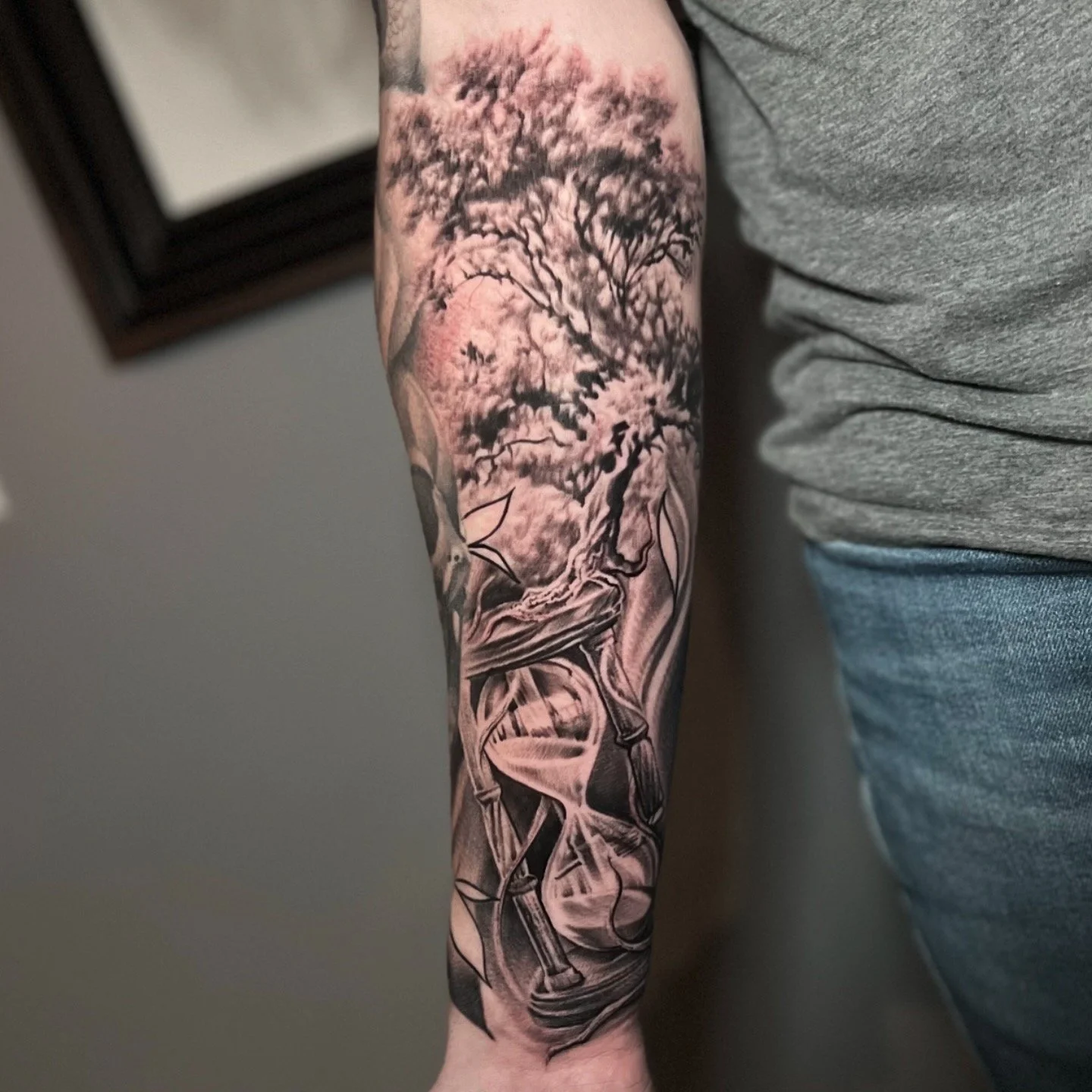 A black and gray tattoo of a blooming tree with pink flowers on a person's forearm.