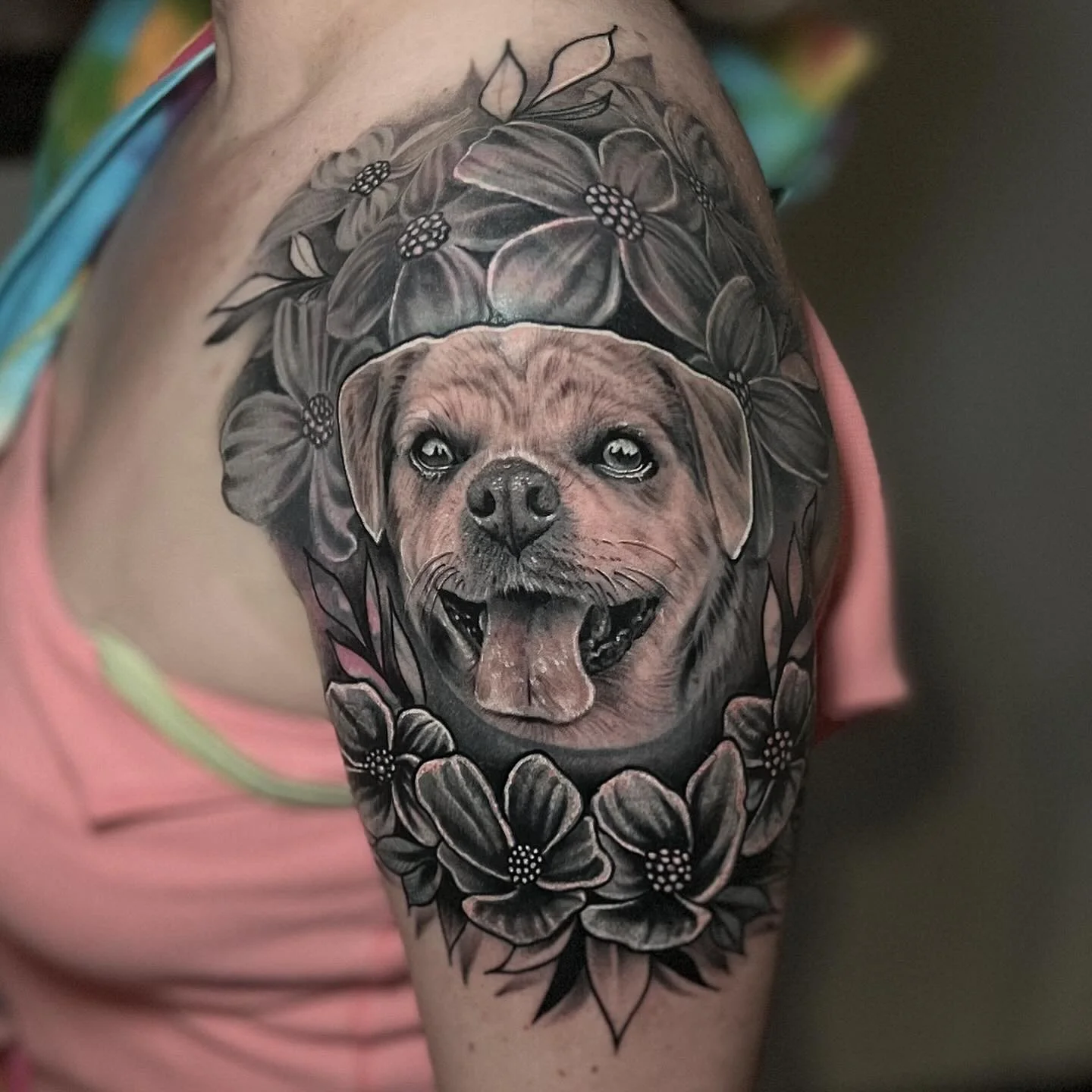 Tattoo of a happy dog's face with open mouth and tongue out, surrounded by detailed black and gray flowers.