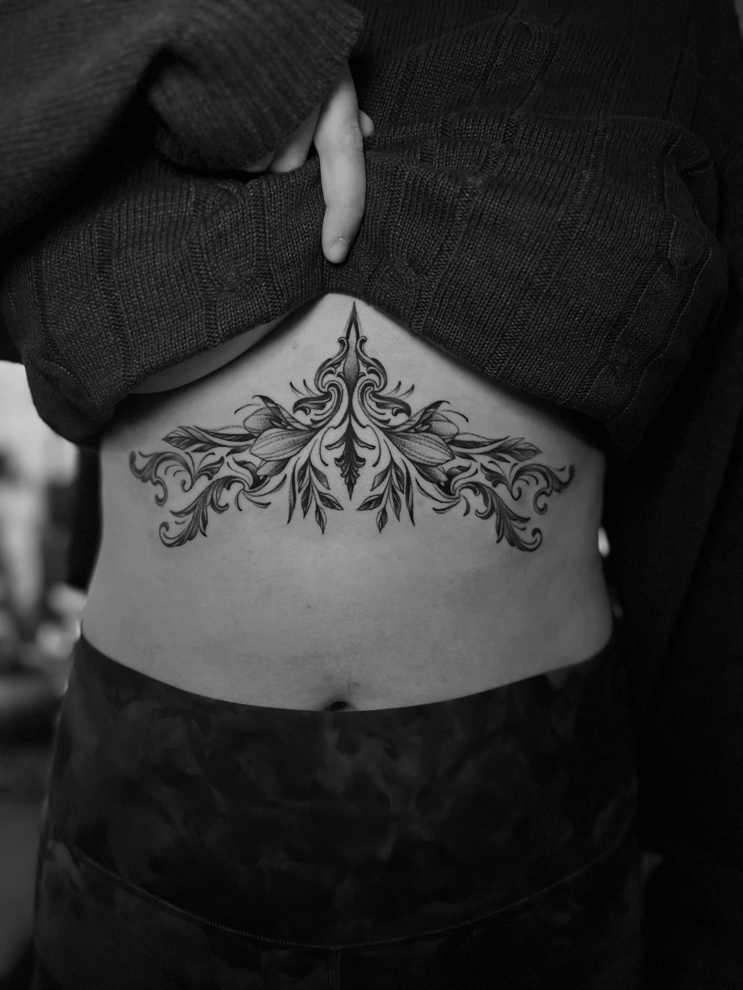 A person showing a detailed floral tattoo on their side, with their clothing partly lifted to reveal the tattoo.