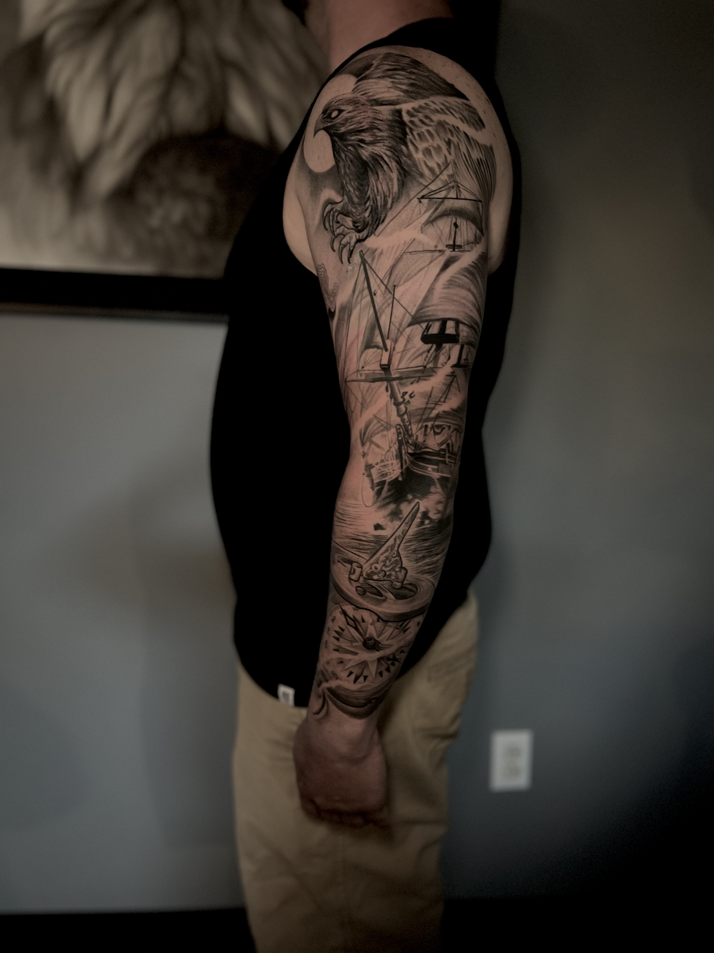 Tattoo of an eagle on the upper arm with a nautical scene including ships, a boat, a compass, and a lighthouse.