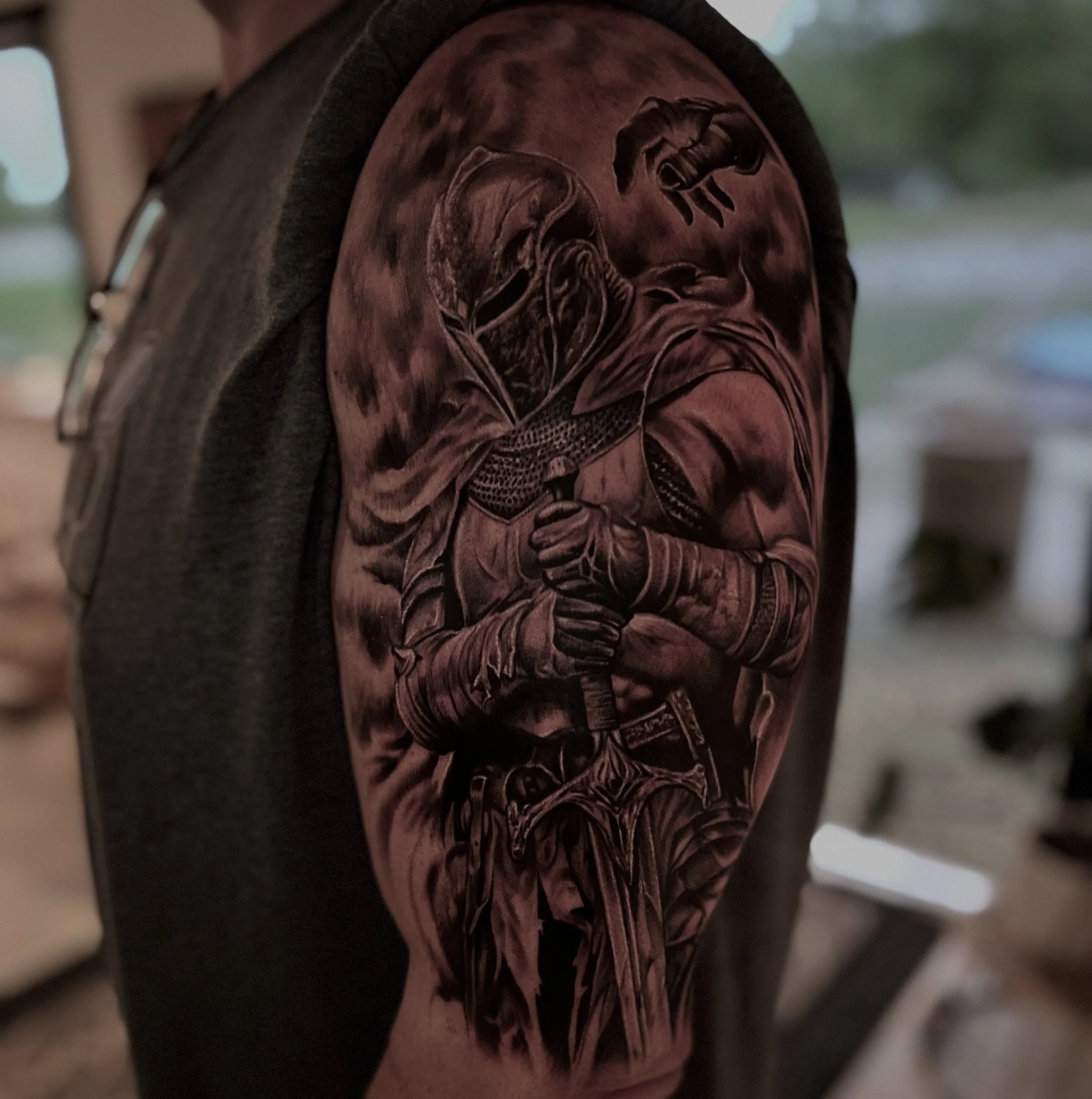 Black and gray tattoo of a knight holding a sword on a person's upper arm.