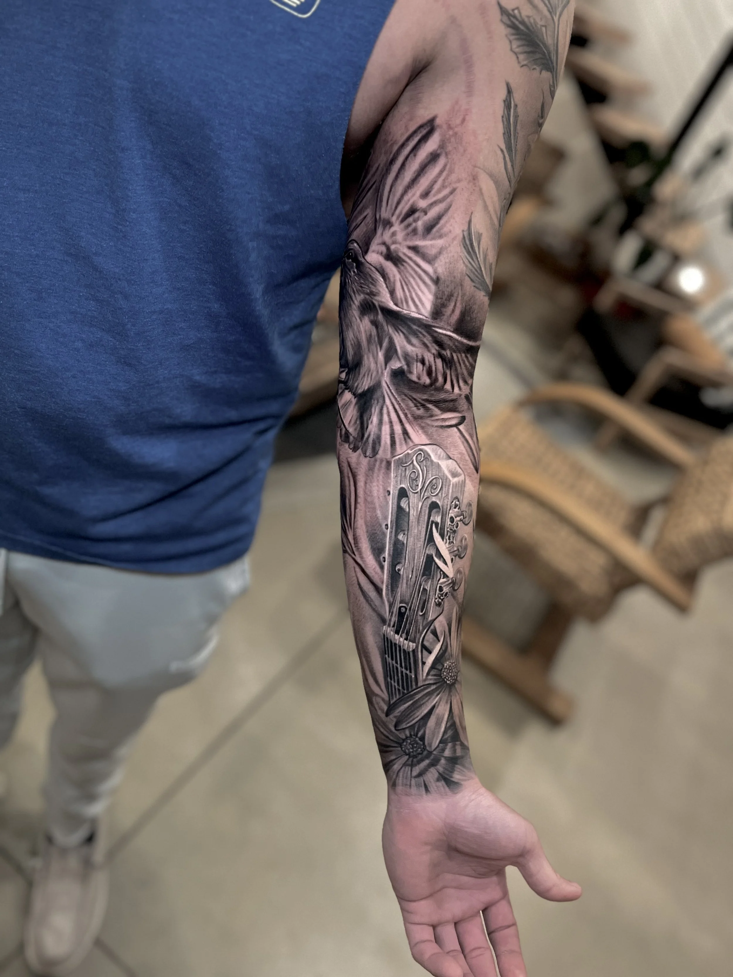 Black and gray tattoo sleeve featuring a bird, a guitar, and floral elements.