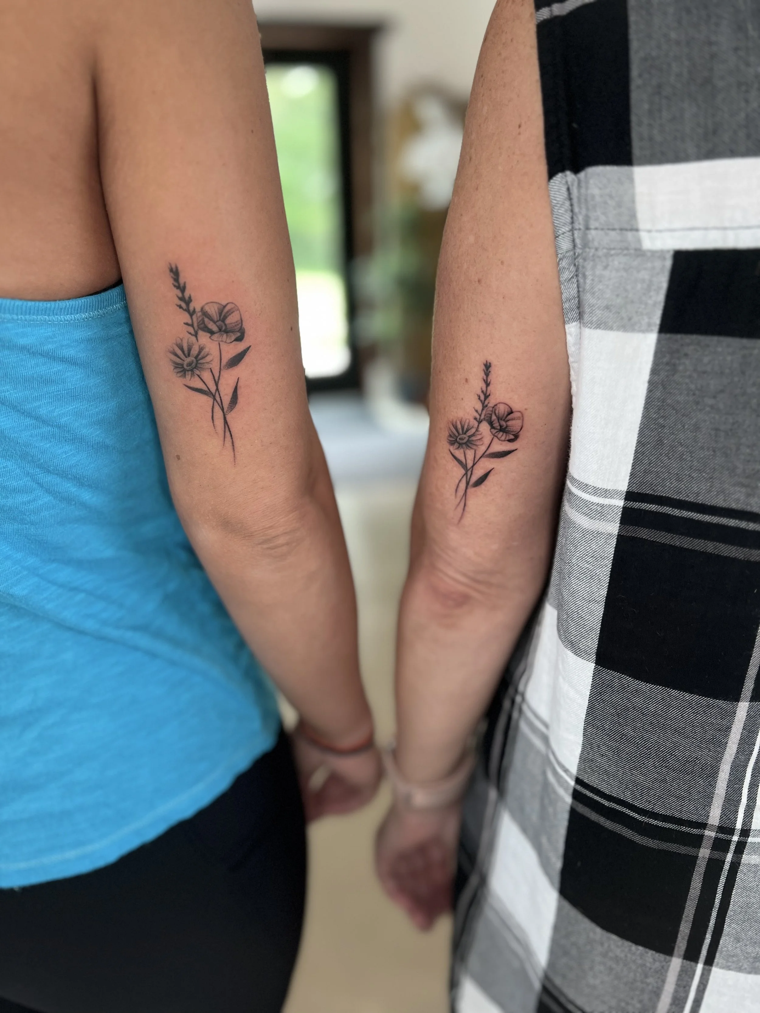 Two people holding hands with matching floral tattoos on their inner wrists.