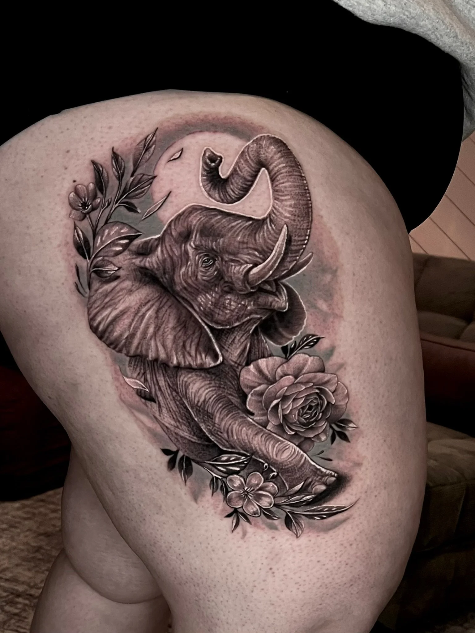 Tattoo of an elephant with floral decorations on a person's thigh.